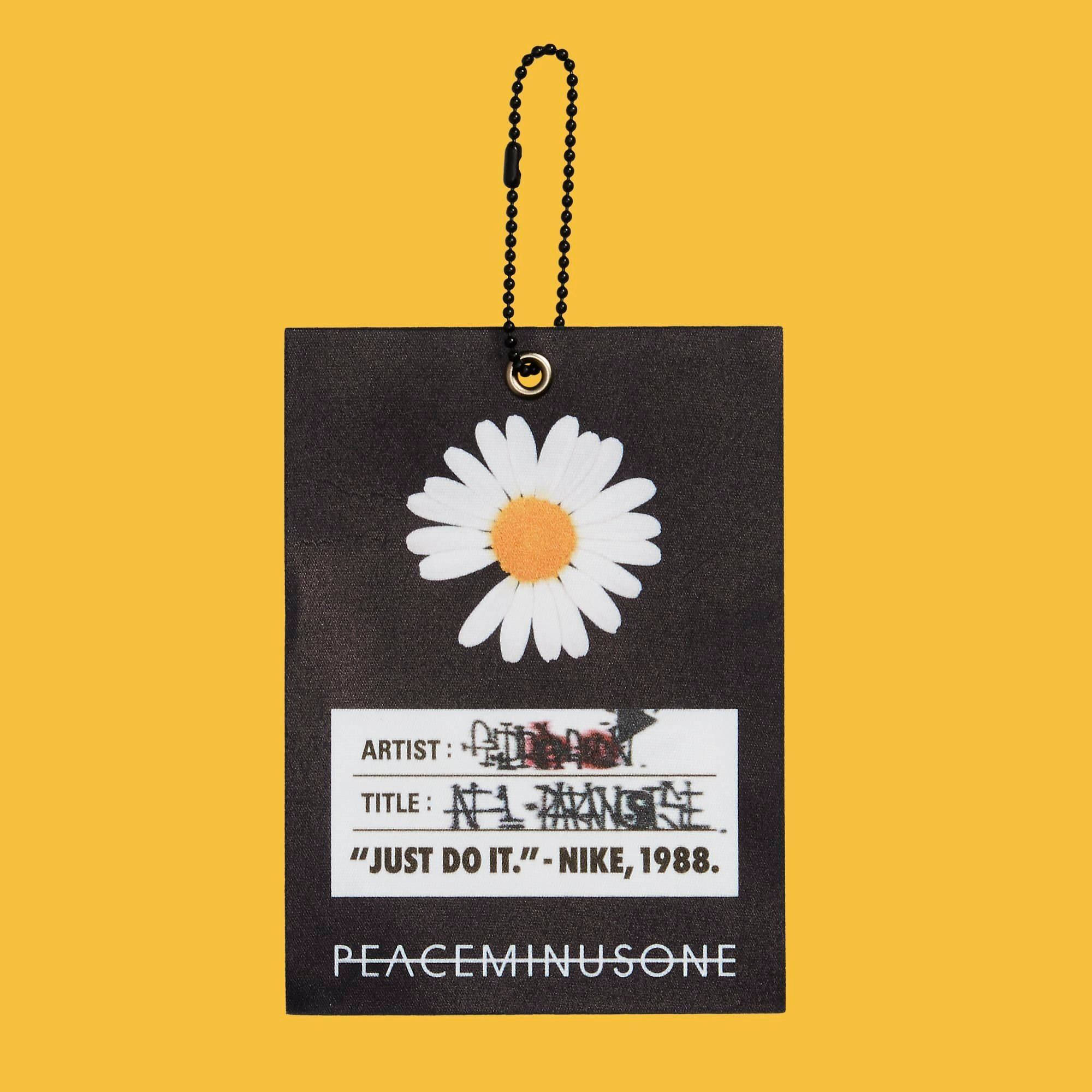 Peaceminusone 黃色背景 壁紙 — 一個黑色標籤，上面有壓花雛菊和塗鴉文字，掛在鮮黃色背景上。