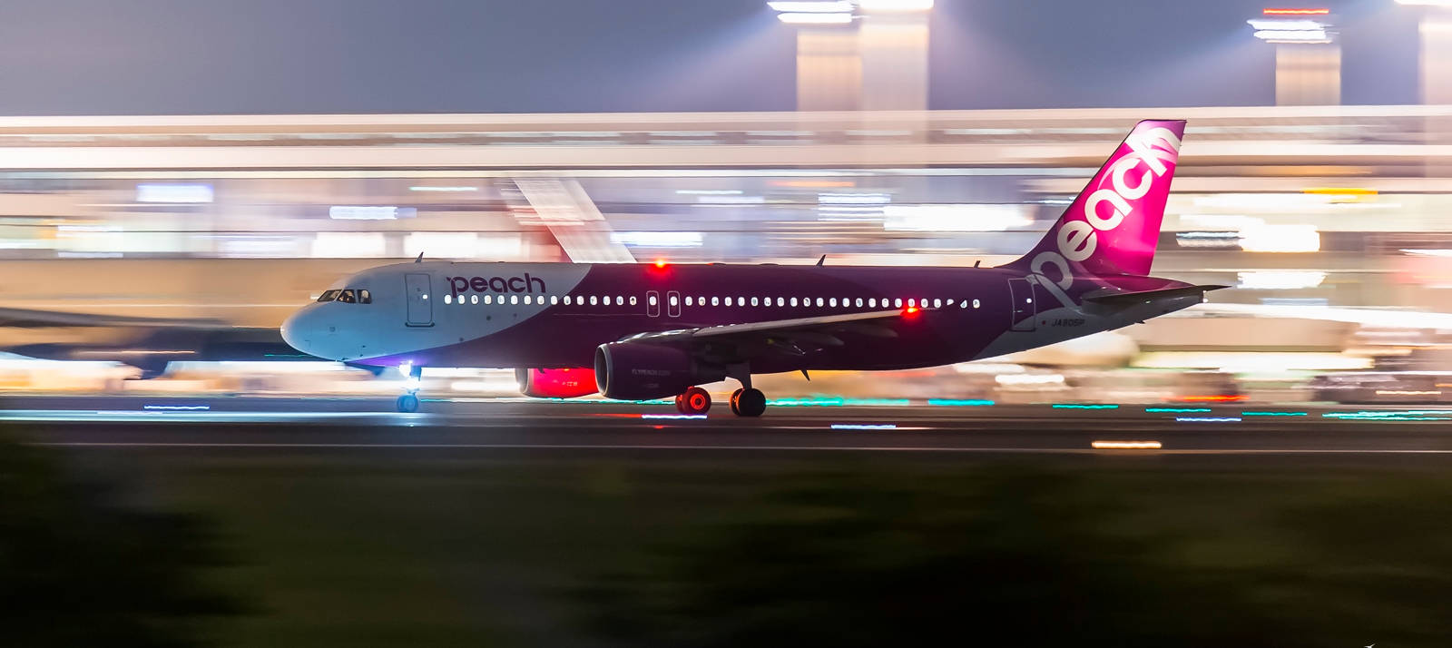 Peach Airlines 飛機在夜間快速移動在跑道上，燈光模糊。