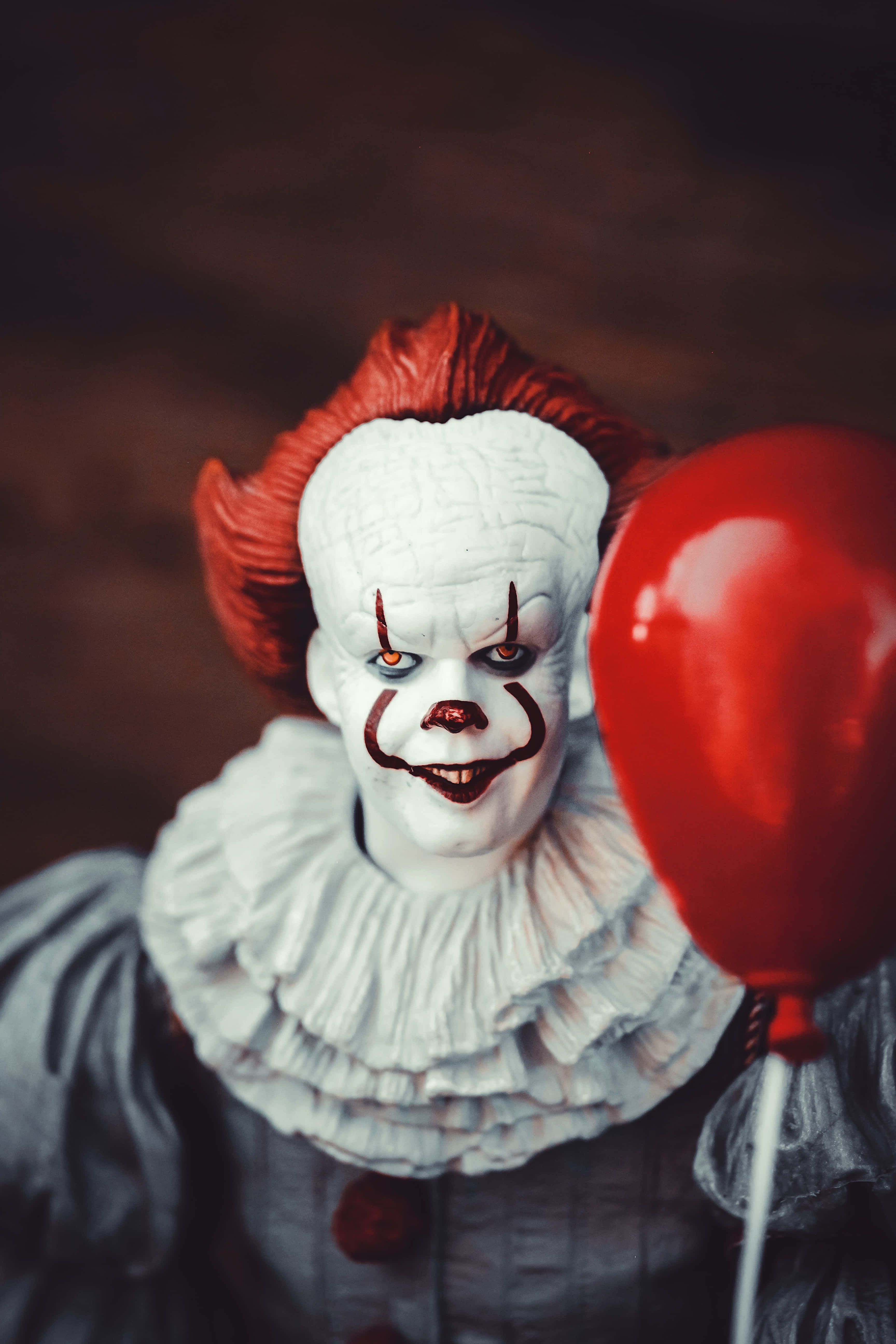 偉大恐怖小丑 Pennywise 圖片 壁紙 — 一個紅髮白臉的可怕小丑，在黑暗背景下拿著一個紅色氣球。
