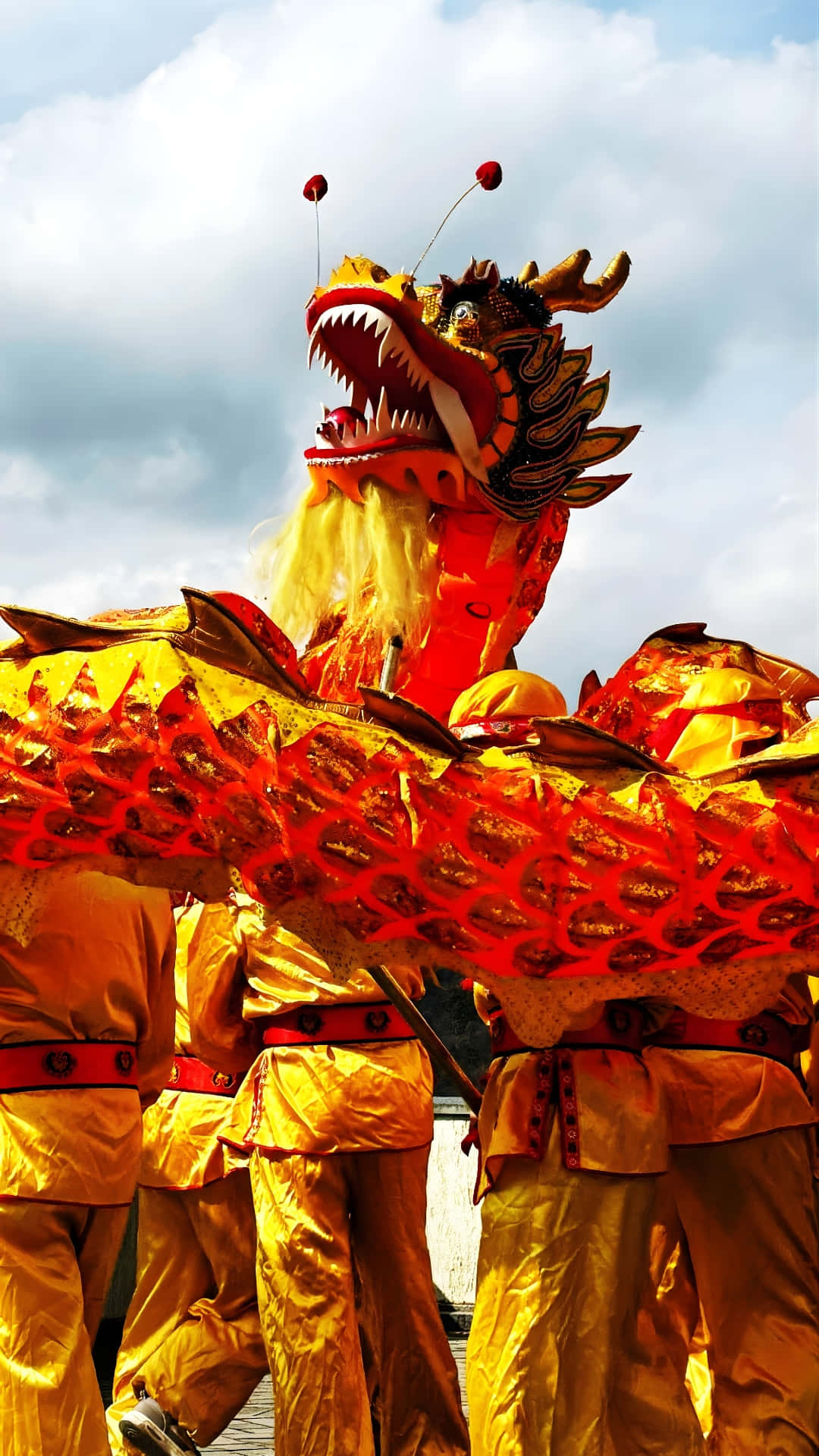  壁紙 — 表演者身穿金色服裝，在陰雲密布的天空下操控著鮮豔的紅金龍偶。