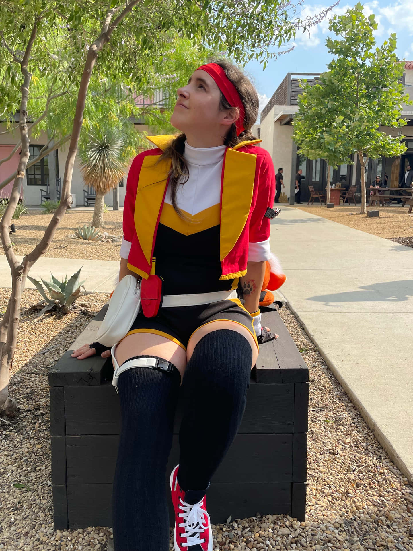  壁紙 — 一個人穿著紅、黃、黑的cosplay服裝，坐在戶外的木長椅上，陽光普照。