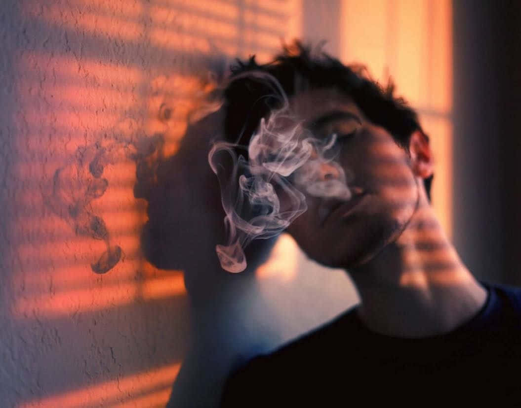 一個人在溫暖的室內光線中呼出煙霧，百葉窗投下陰影。