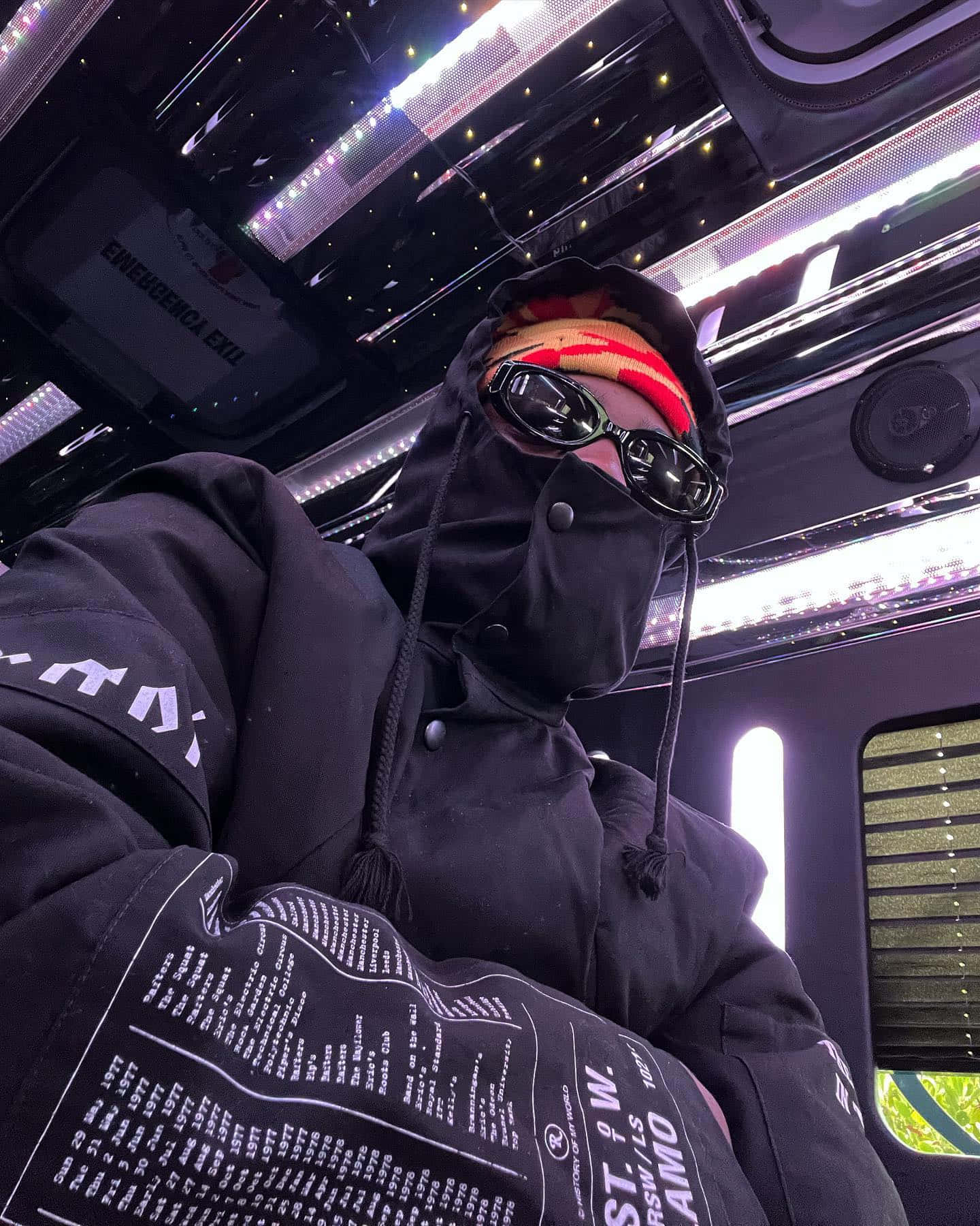  壁紙 — 一個穿著黑色連帽衫和口罩的人在一輛帶有發光LED燈和星空天花板的豪華車內擺姿勢。