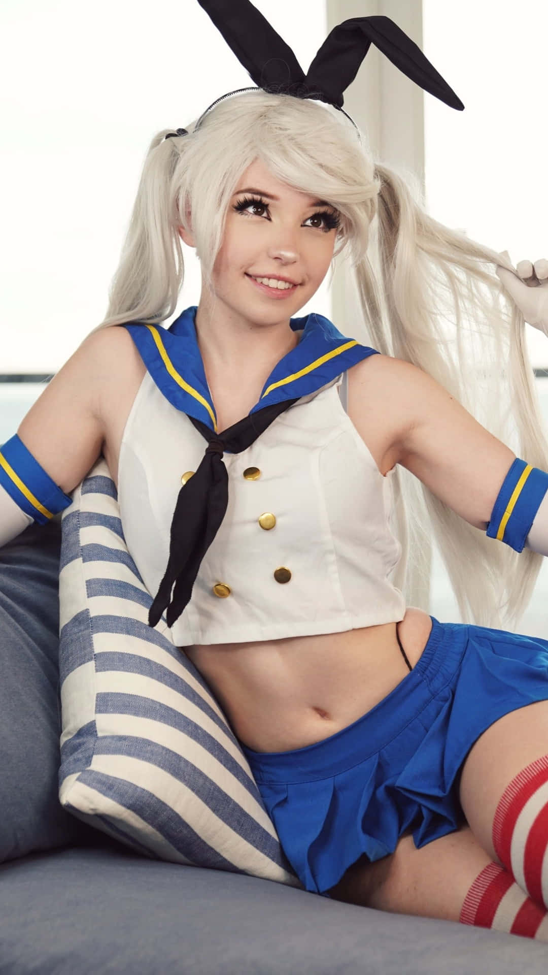  壁紙 — 一個穿著兔女郎水手服的人微笑著躺在條紋枕頭上。