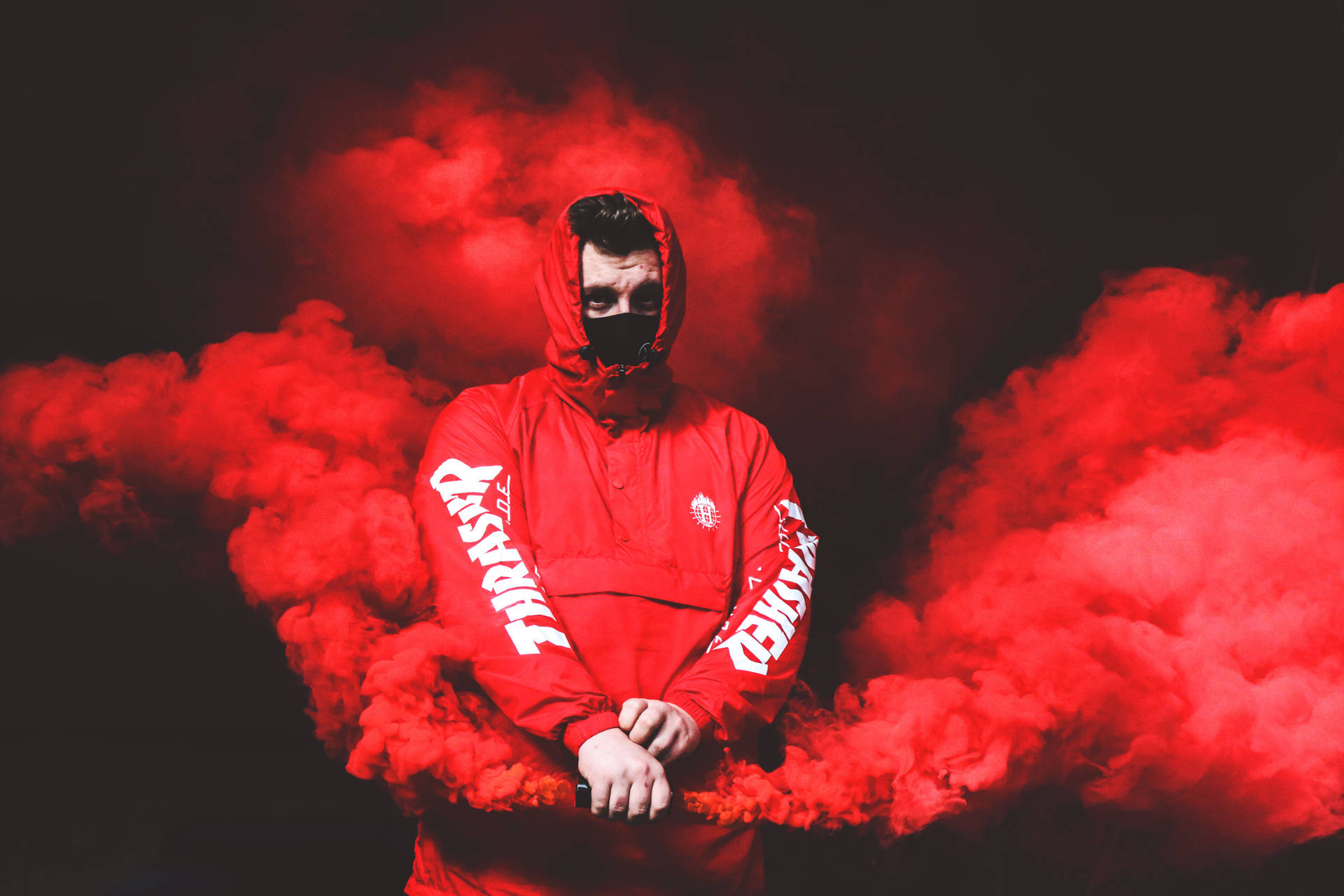紅 hood 救援 壁紙 — 一個人穿著紅色連帽衫和黑色口罩，站在黑暗背景中，被旋轉的紅色煙霧包圍。