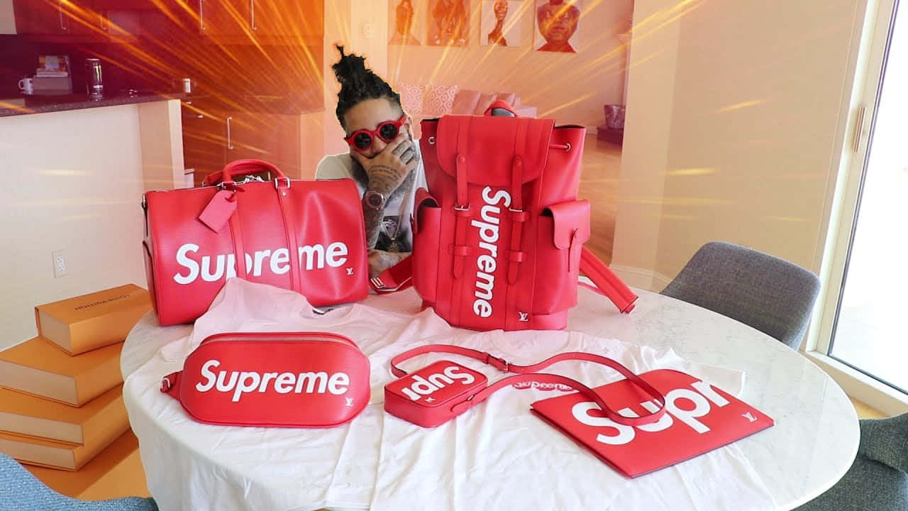 戴紅色太陽眼鏡嘅人喺有紅色 Supreme 品牌手袋同盒嘅枱後面。