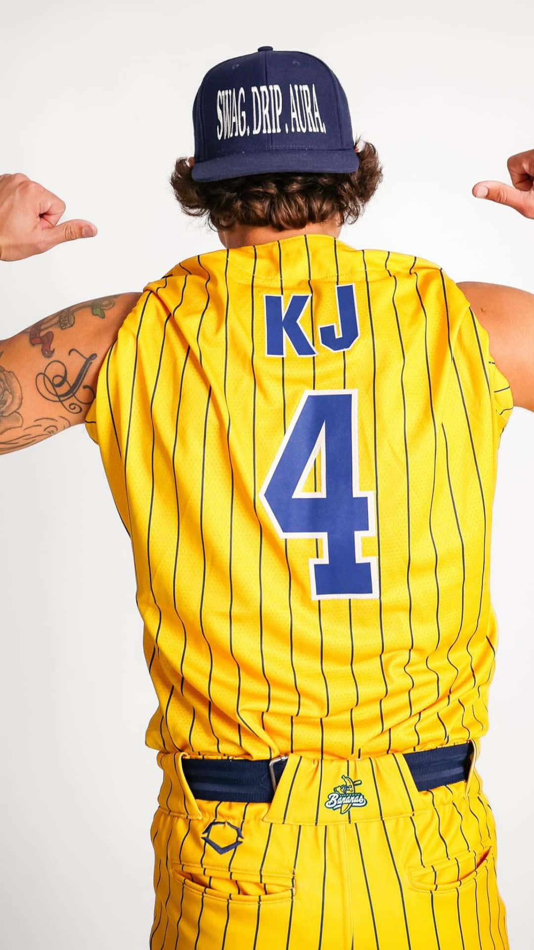  壁紙 — 一名身穿黃色細條紋棒球服的人，背後有「KJ 4」，帽子寫著「SWAG DRIP AURA」，指著自己的肩膀。