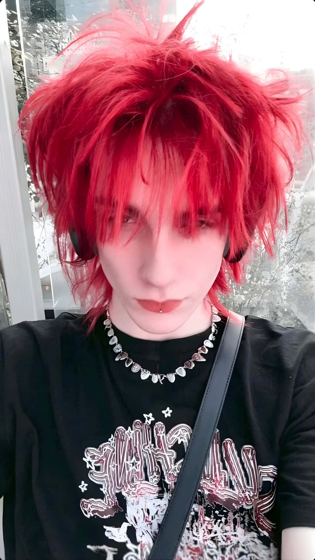  壁紙 — 一個擁有鮮紅色尖刺頭髮和深色化妝的人，穿著黑色圖案T恤和銀色鏈條項鍊，強烈地凝視著鏡頭。