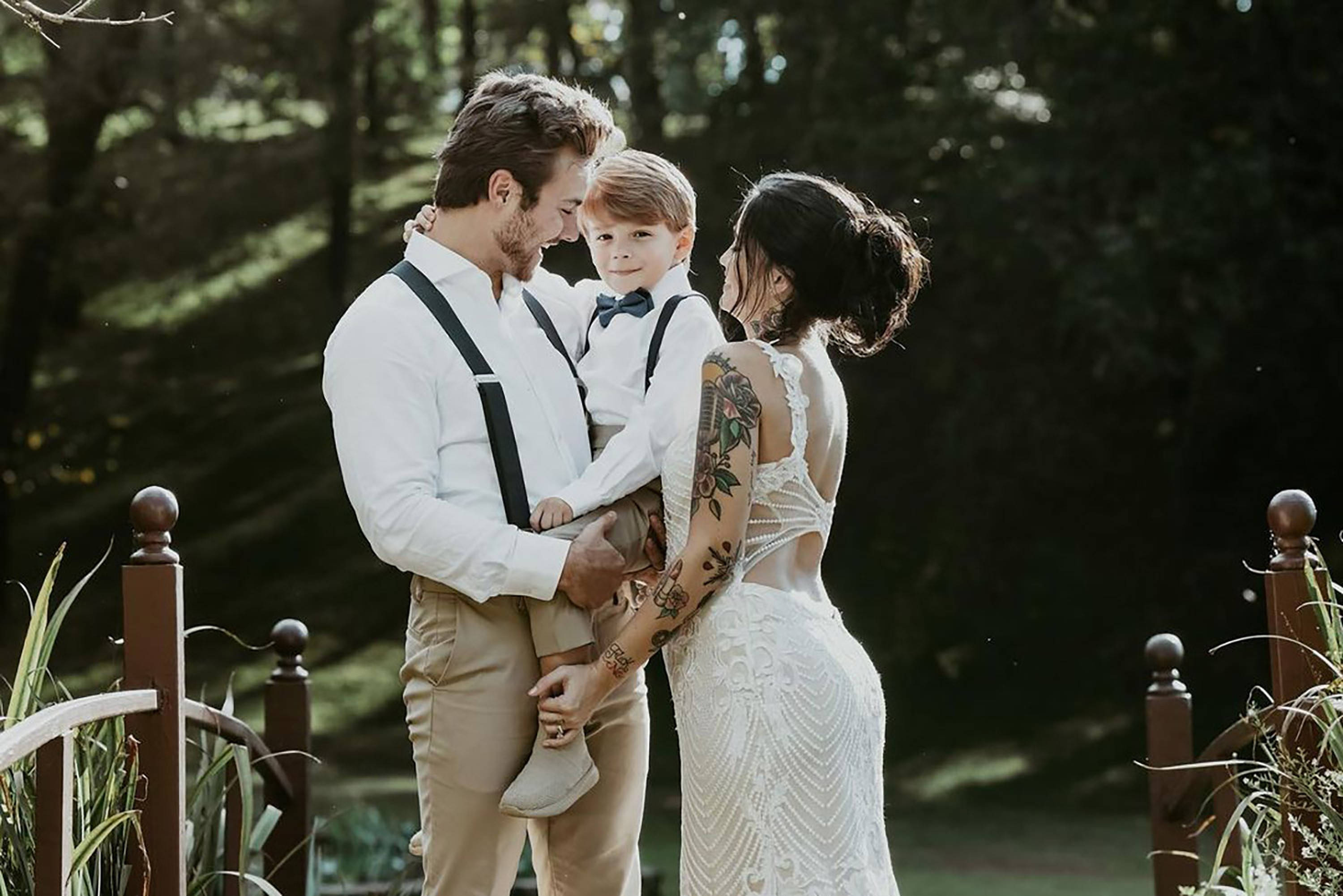 Peyton Meyer 婚禮 壁紙 — 一家三口在陽光照耀的樹木環繞的木橋上分享溫馨時刻。