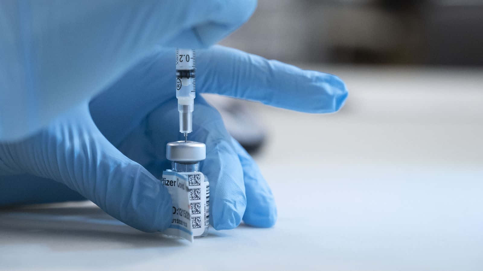 戴手套的手用注射器從藥瓶中抽取疫苗。
