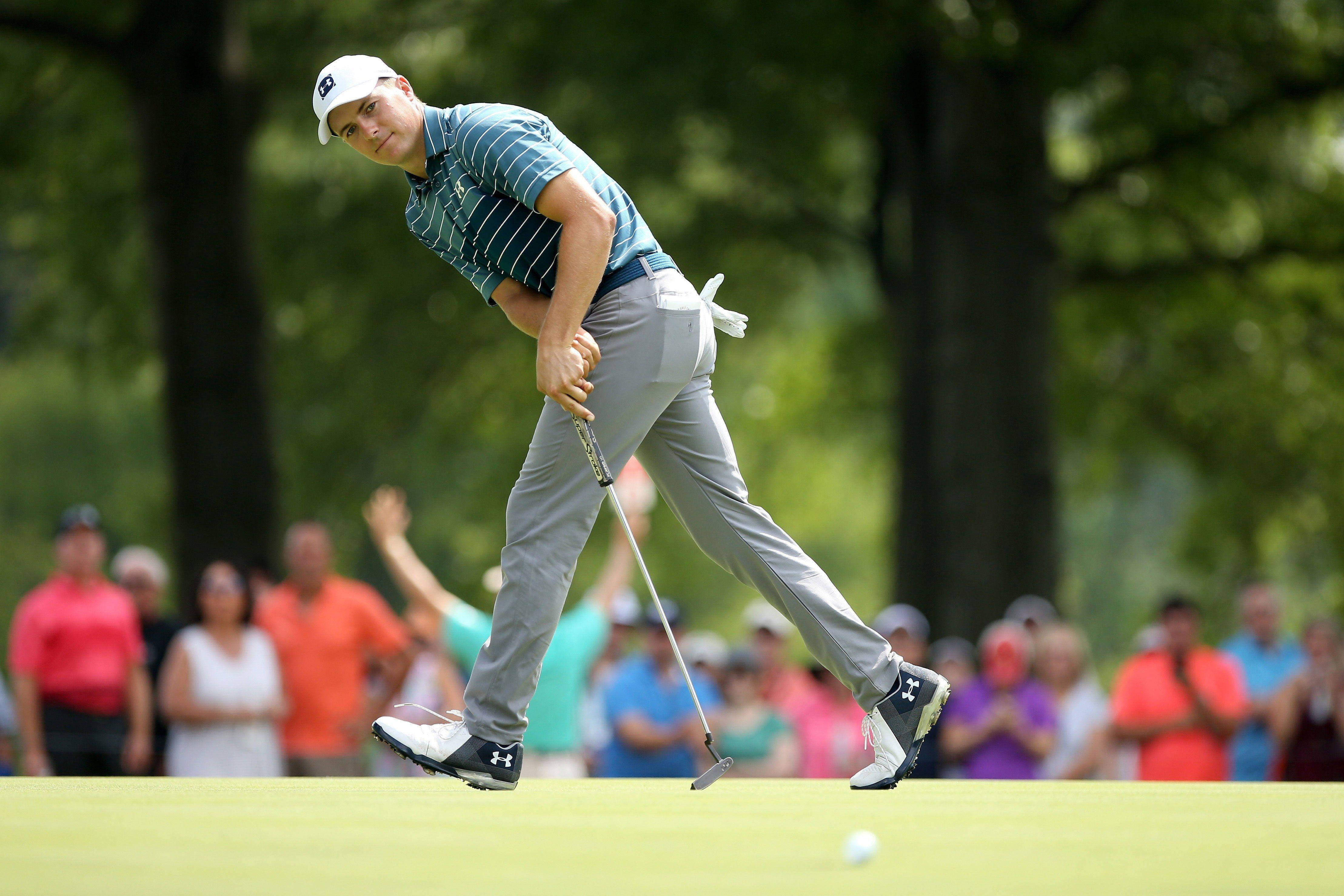 PGA WGC-布里奇斯通 斯皮思 壁紙 — 一位專注的高爾夫球手，身穿條紋襯衫和灰色長褲，在充滿活力的果嶺上推桿，背景中的觀眾模糊不清。