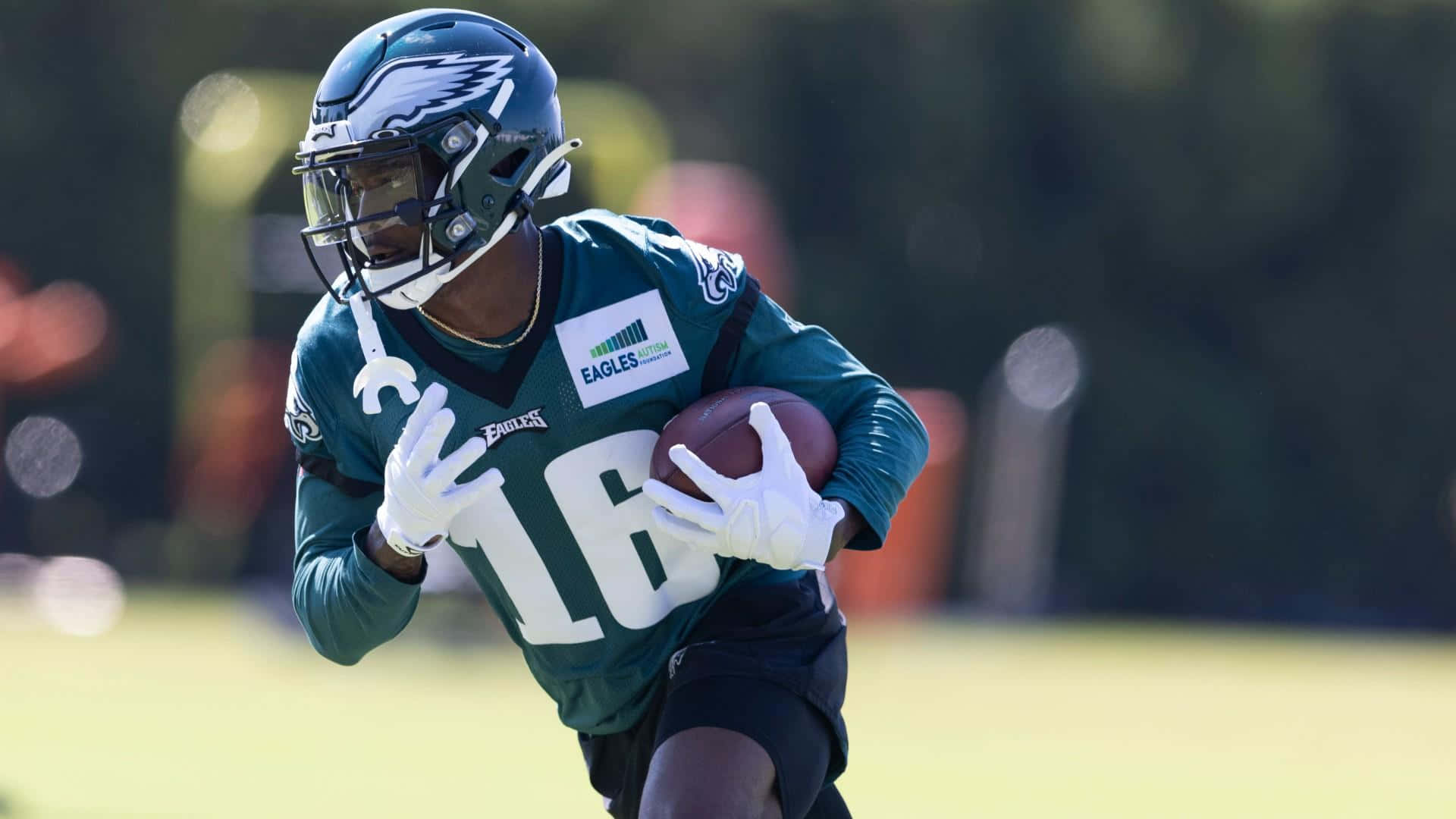  壁紙 — 一名身穿青綠色球衣的費城老鷹隊美式足球員，在陽光明媚的戶外訓練中帶球衝刺。