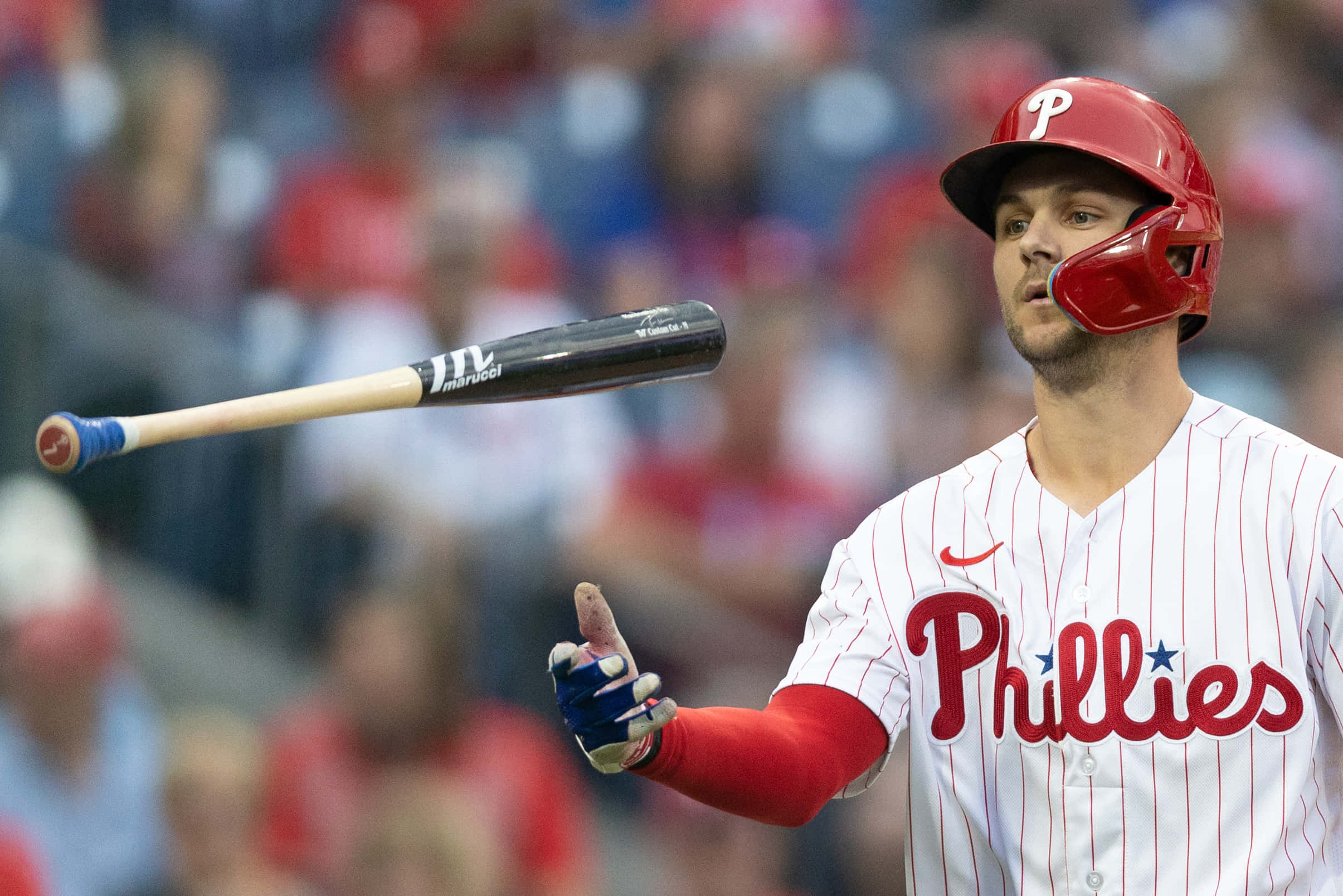 Trea Turner Phillies 桌布 壁紙 — 一名費城費城人棒球選手戴著紅色頭盔、身穿條紋制服，在比賽中揮棒後擲出球棒。