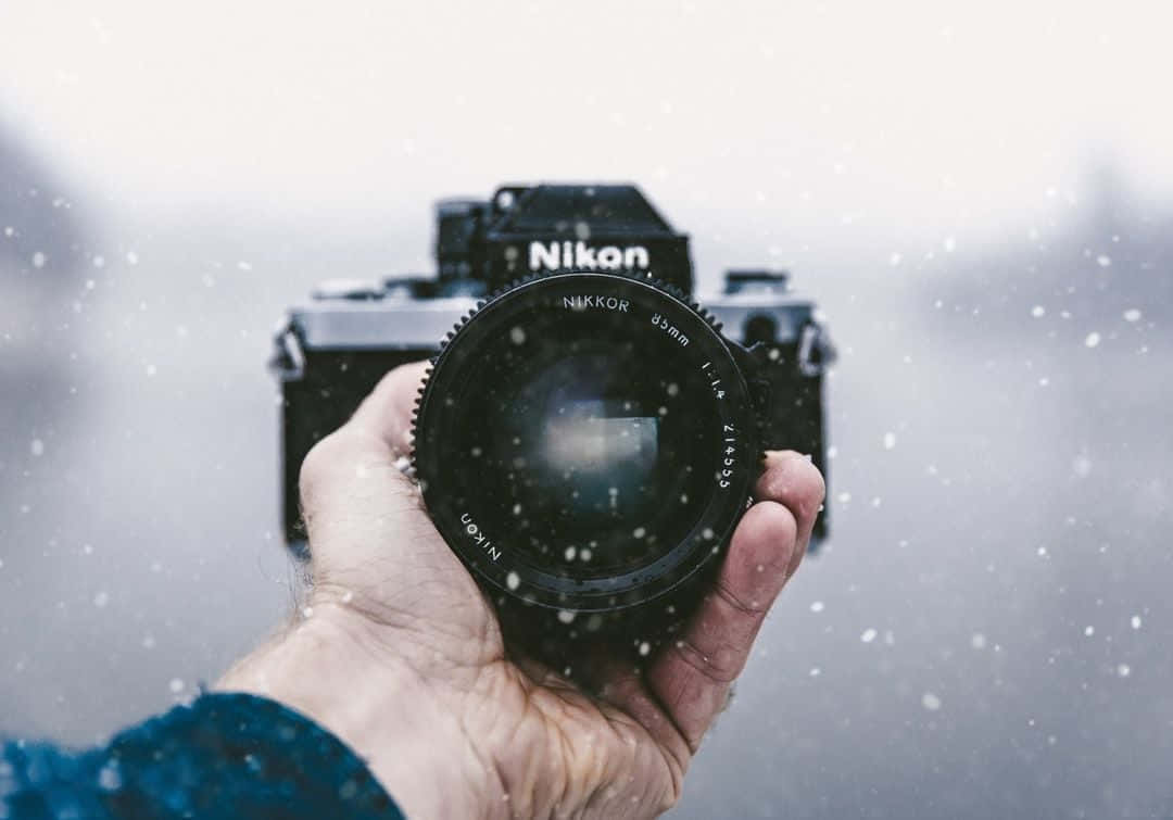 手在飄雪中拿著一部 Nikon 菲林相機。