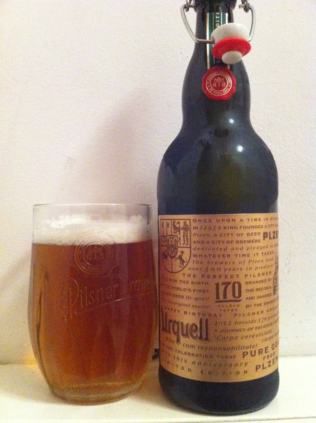 一瓶Pilsner Urquell啤酒旁邊放著一杯裝滿琥珀色啤酒和泡沫的玻璃杯。