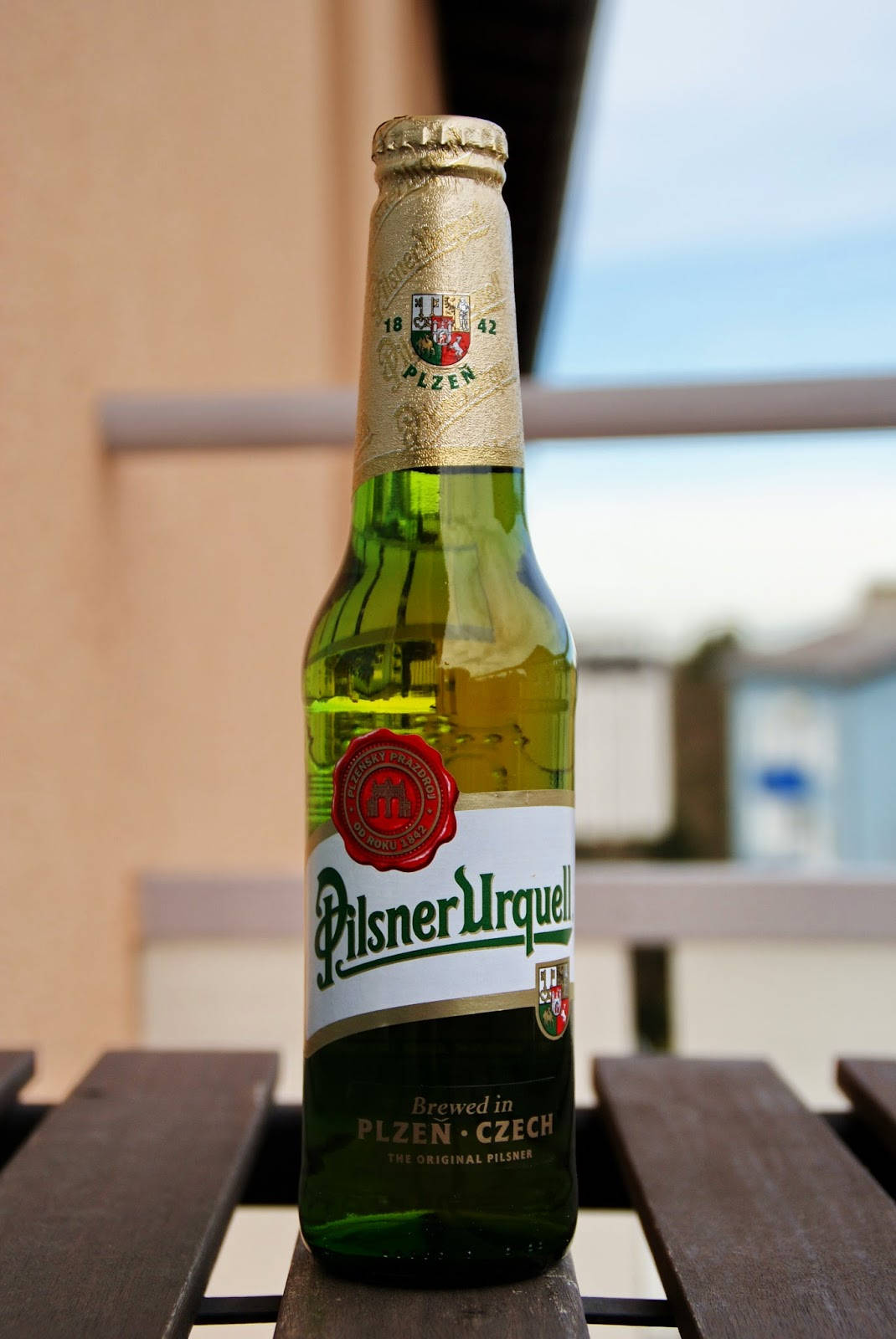 一個綠色嘅Pilsner Urquell啤酒樽喺戶外木桌上。