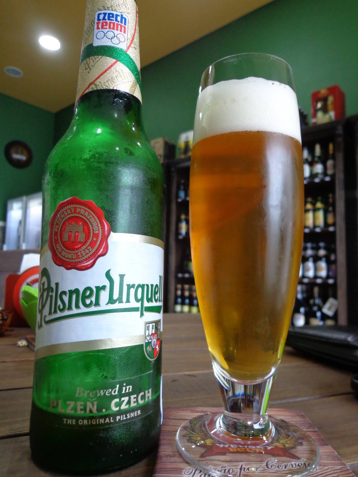 酒吧木製吧檯上的一支綠色Pilsner Urquell啤酒瓶和一杯滿的啤酒。
