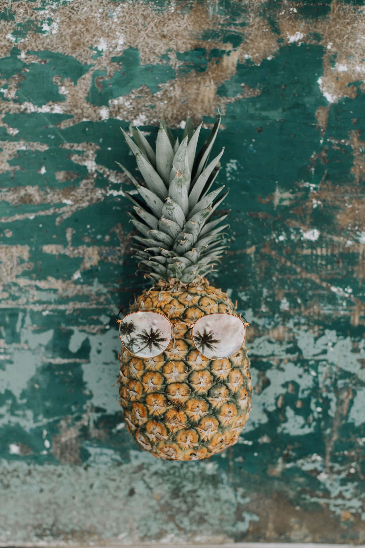 一個戴著太陽眼鏡的菠蘿在剝落的綠色牆上。