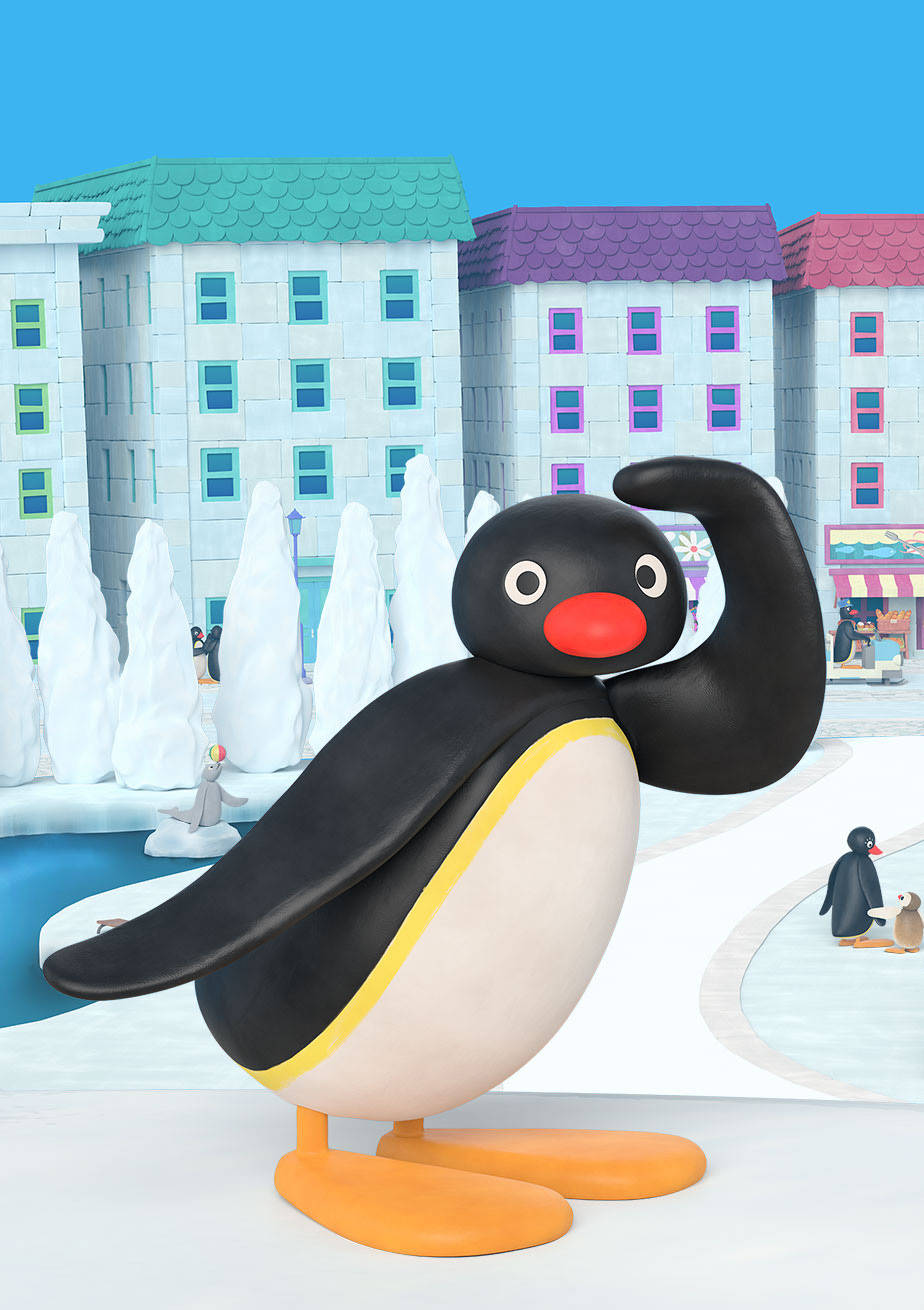 Pingu在城市 壁紙 — 企鵝Pingu在雪城裡自豪地彎曲手臂，背景有色彩繽紛的建築和冰雕。
