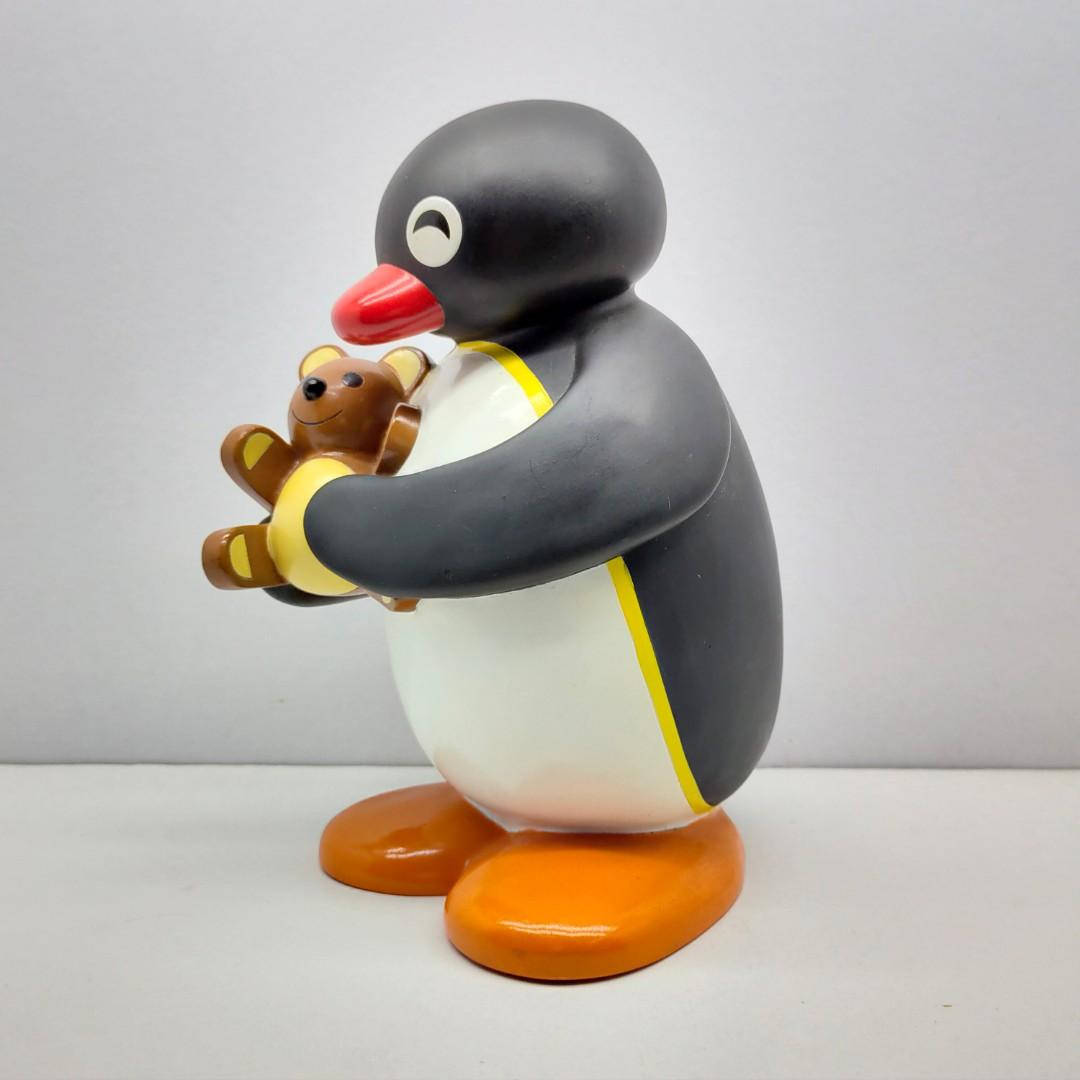 Pingu抱泰迪熊 壁紙 — 一個光滑的塑膠企鵝公仔在純白色背景前抱著一隻小棕色泰迪熊。