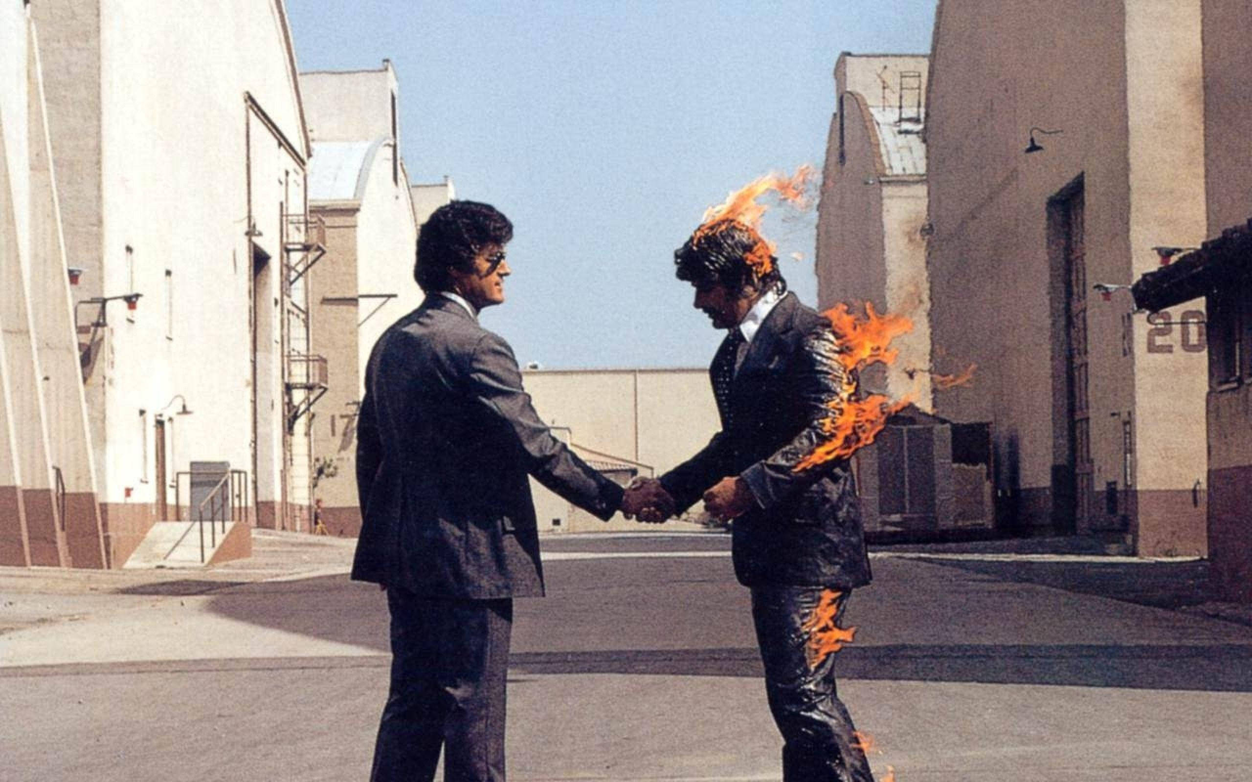 Pink Floyd《Wish You Were Here》4K專輯封面 壁紙 — 兩名身穿西裝的男子在後巷握手，其中一人被火焰吞噬，在明亮的日光下。