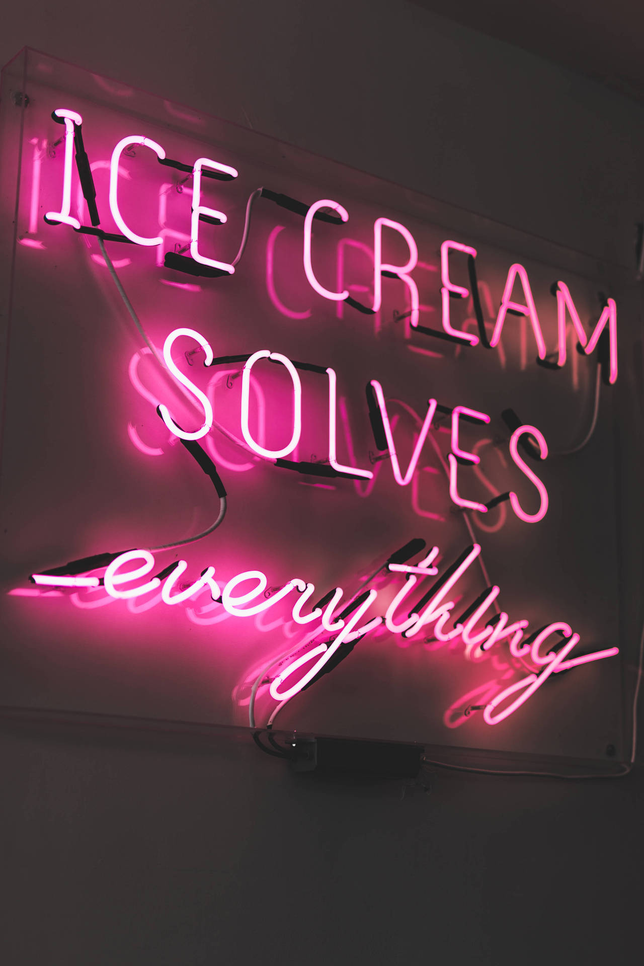 粉紅色霓虹燈牌，上面寫著 ice cream solves everything，在深色牆壁上。