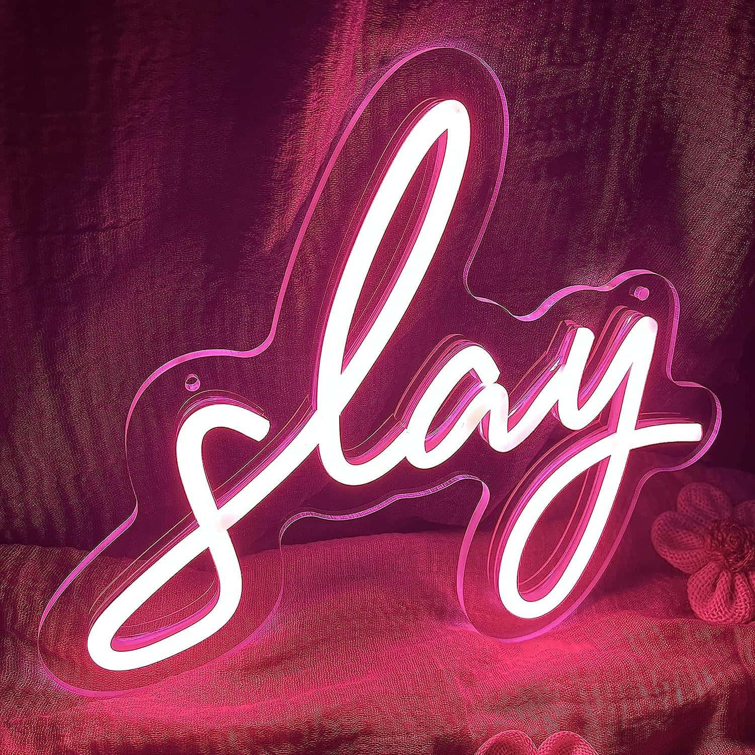  壁紙 — 一個發光的粉紅色霓虹燈牌，拼出「slay」字樣，放置在帶有紋理的布料表面上，周圍光線柔和。
