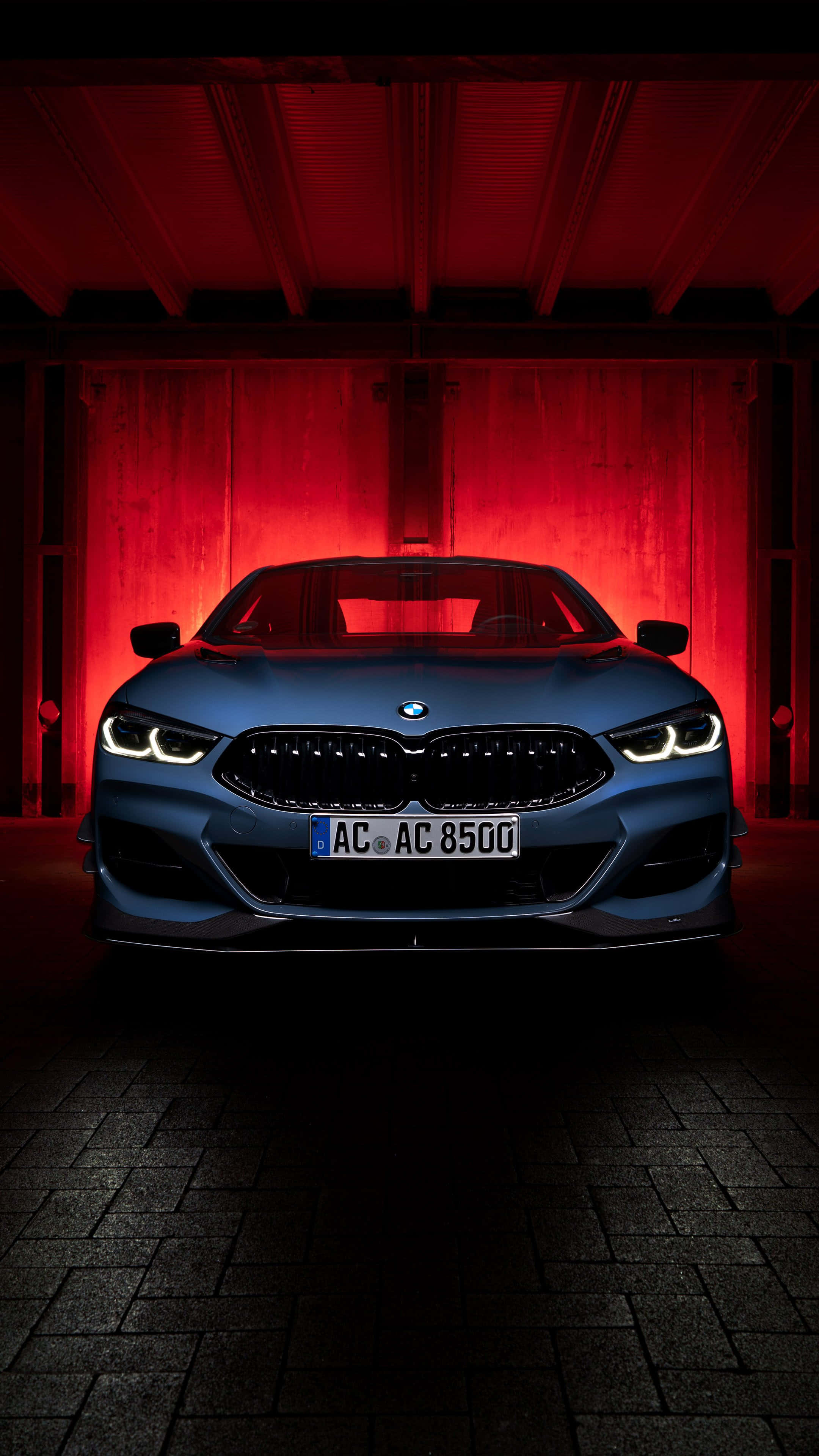 高雅力量 — Pixel 3 BMW 背景 壁紙 — 一輛時尚的藍色BMW跑車在黑暗的工業車庫中，在戲劇性的紅色燈光下閃耀。