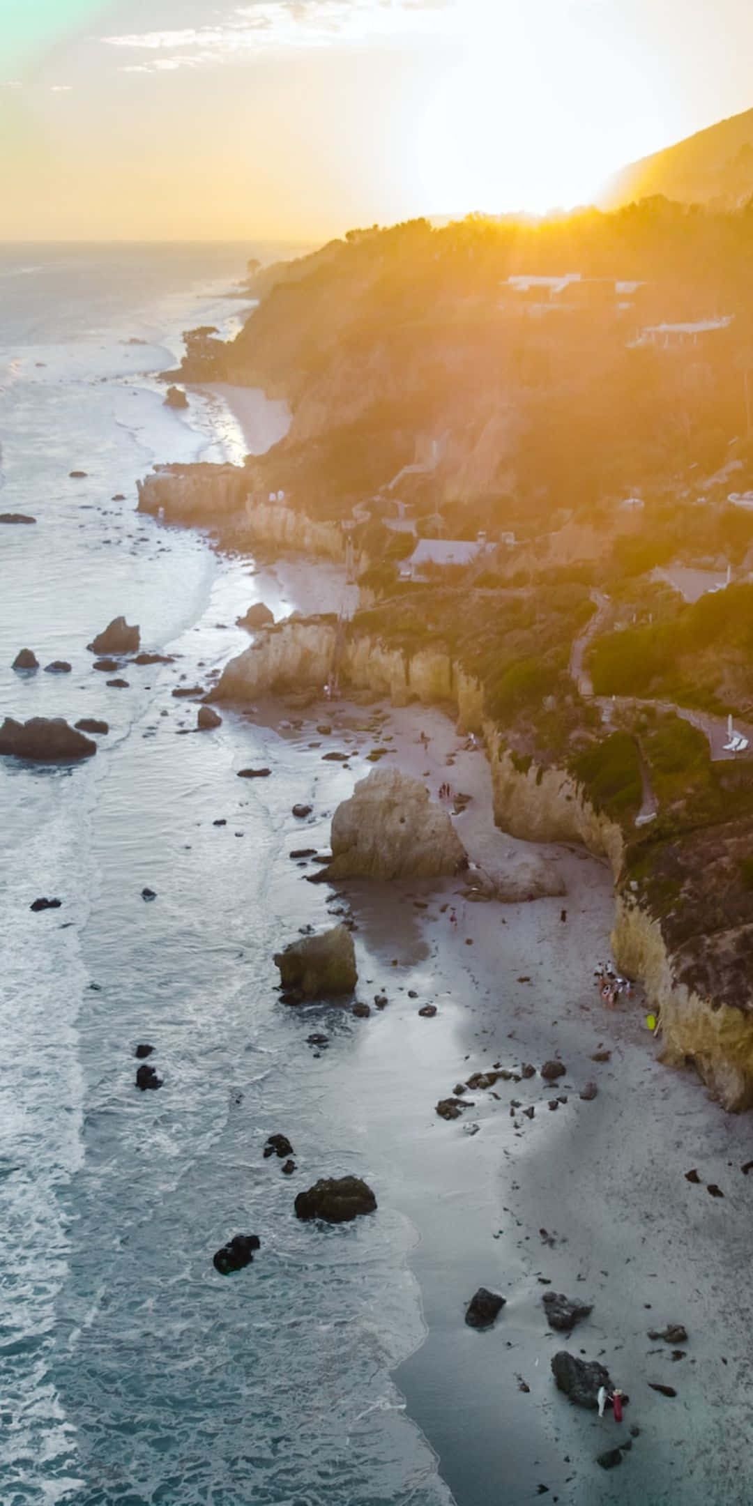 岩石海灘 Pixel 3 Malibu 背景 壁紙 — 陽光普照的海岸懸崖鳥瞰圖，藍綠色海水拍打岩石海岸，散落著海灘遊客。