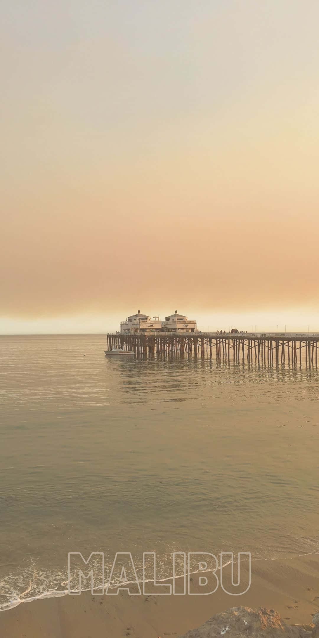 遠眺咖啡館 Pixel 3 Malibu 背景 壁紙 — 寧靜的馬里布碼頭在柔和的金色日落天空下延伸至平靜的海水。