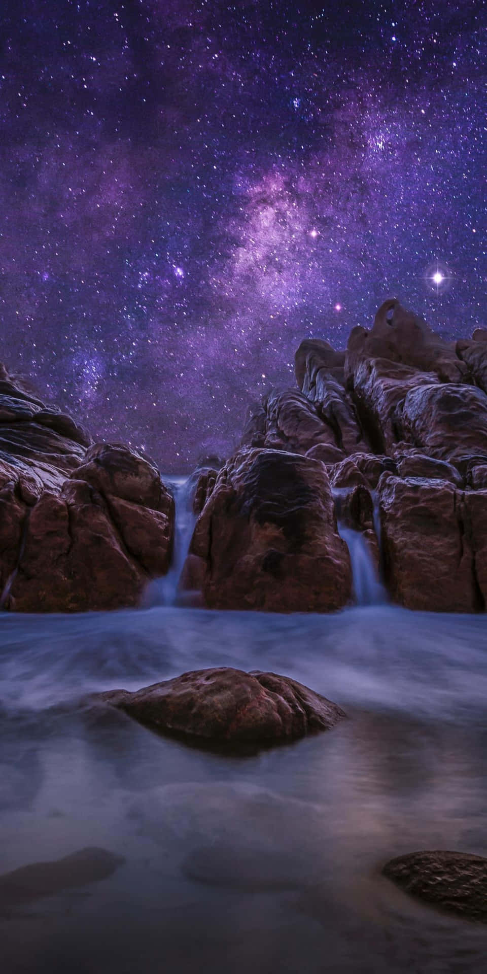 瀑布在紫色星空下在岩石之間流動。
