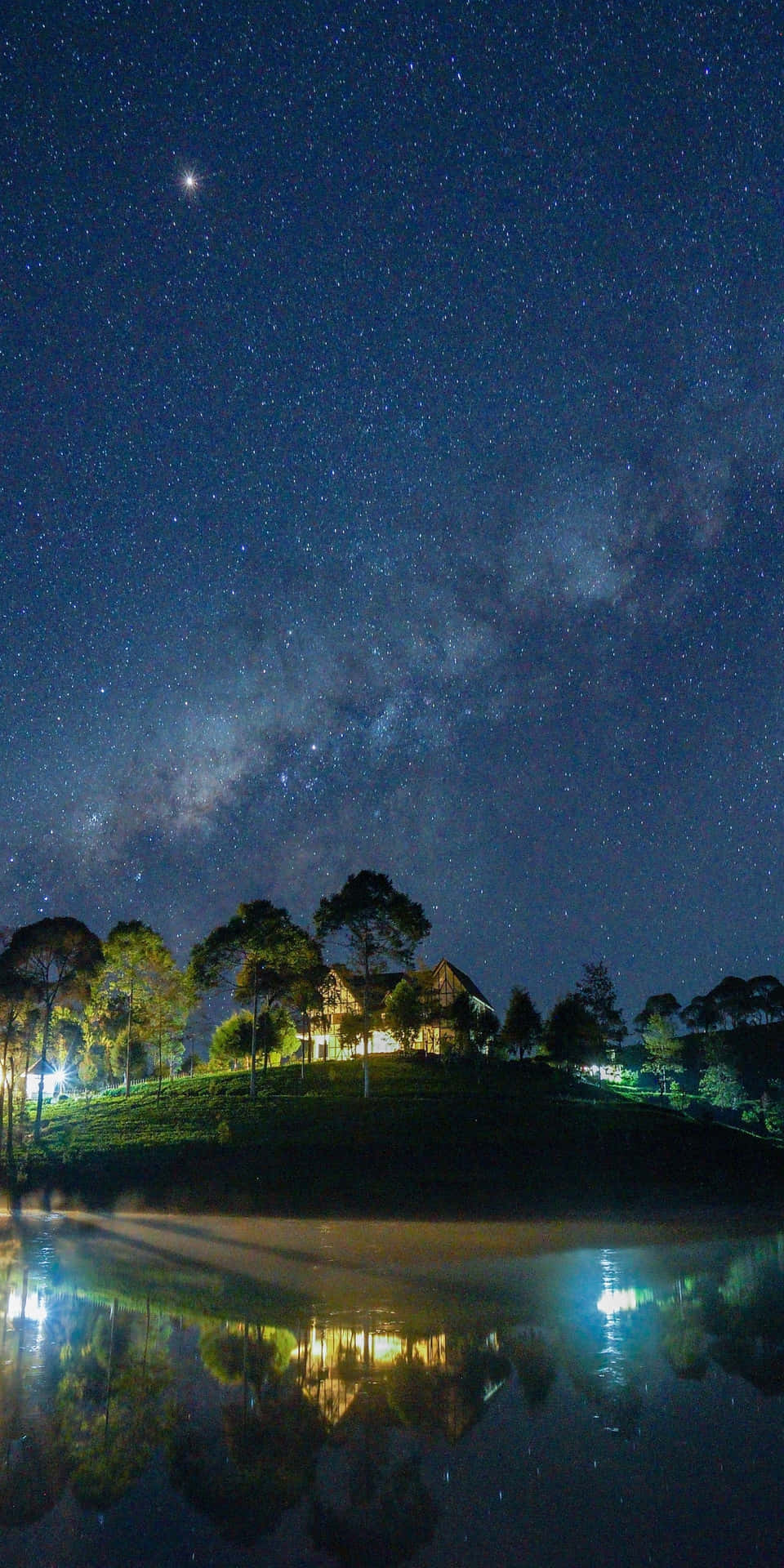 山上的房子在星空和銀河下的水中倒映。