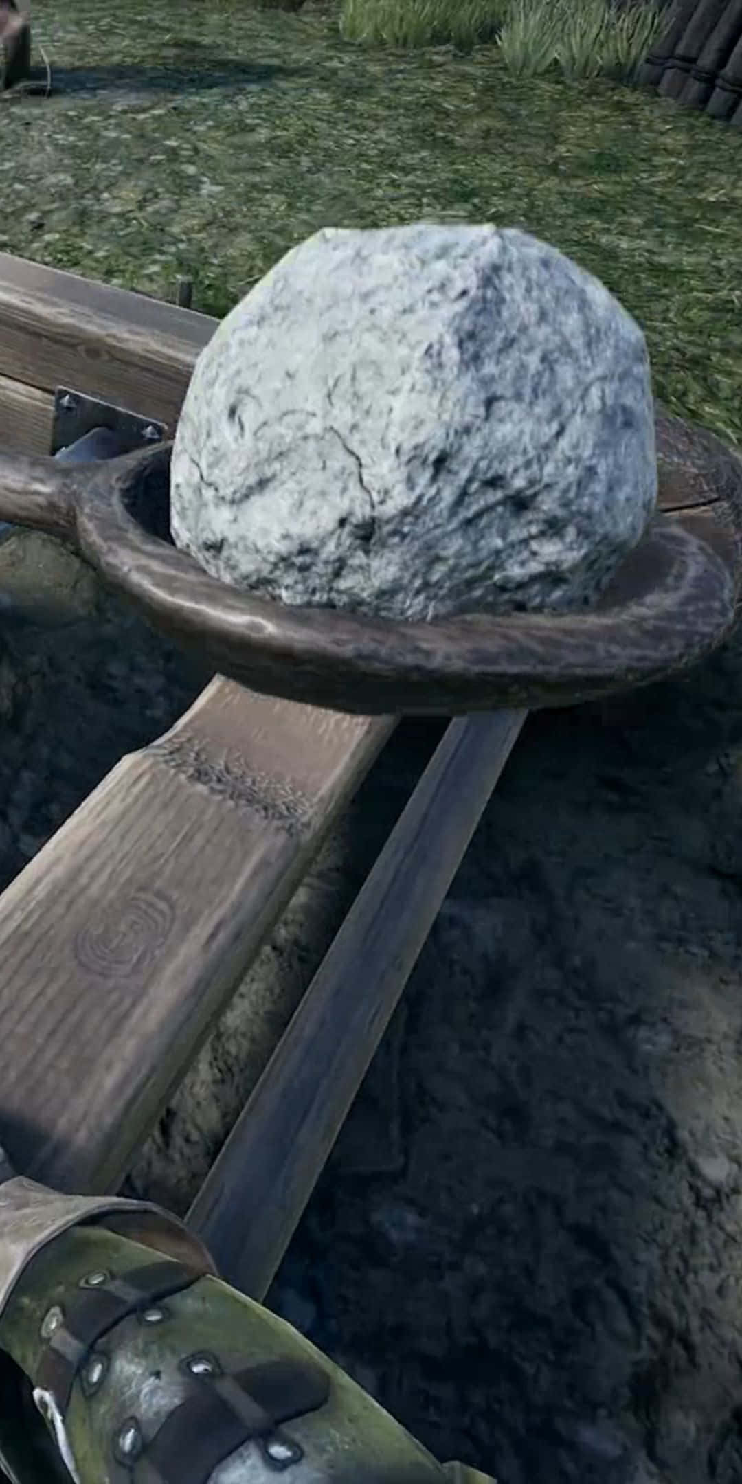 Pixel 3 與《Mordhau》的清晰銳利畫面 壁紙 — 一塊巨大的灰色岩石放在一個設置在草地戶外區域的木製投石機的彈弓中。