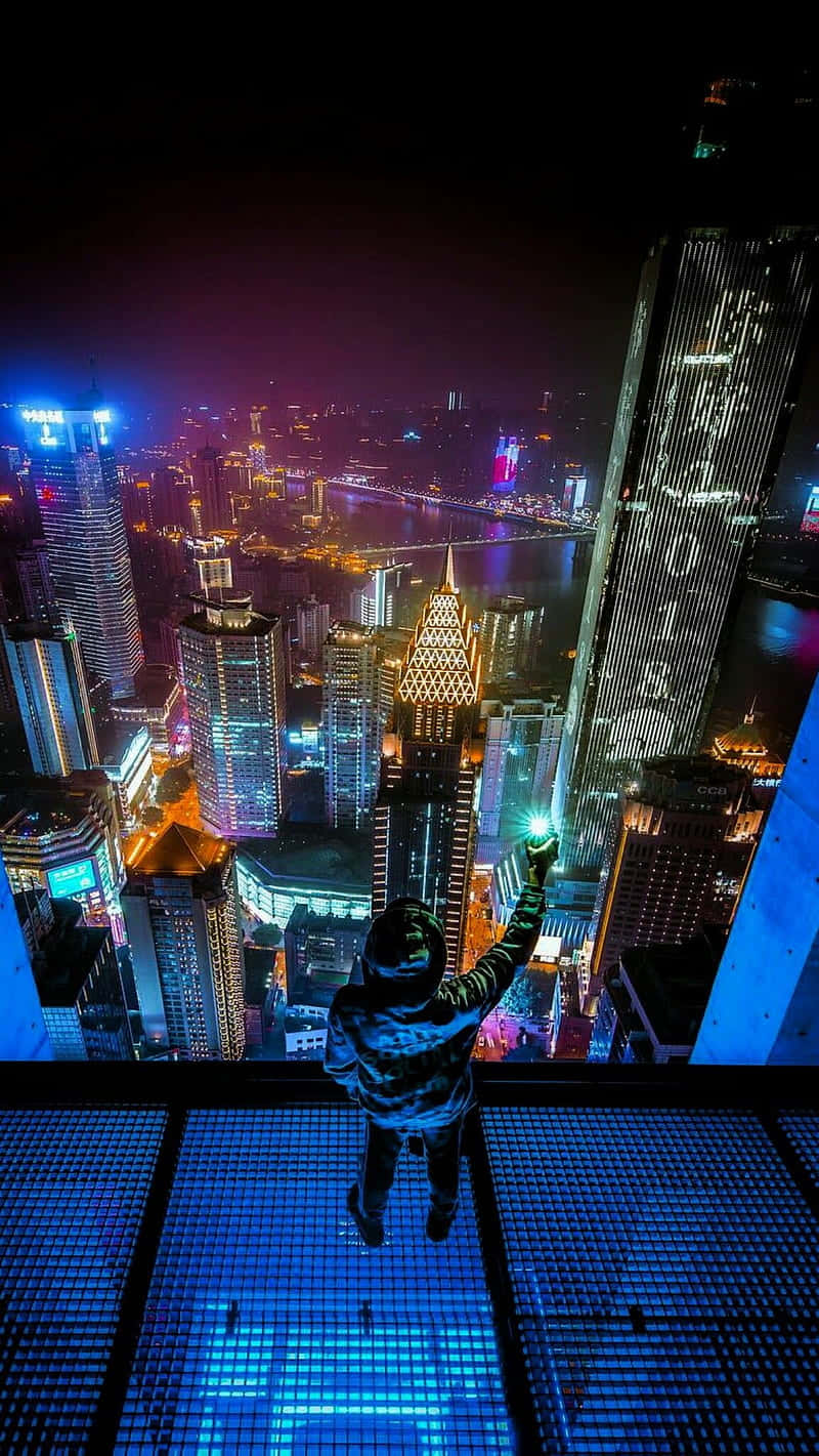 夜晚喺玻璃露台上俯瞰發光城市嘅人
