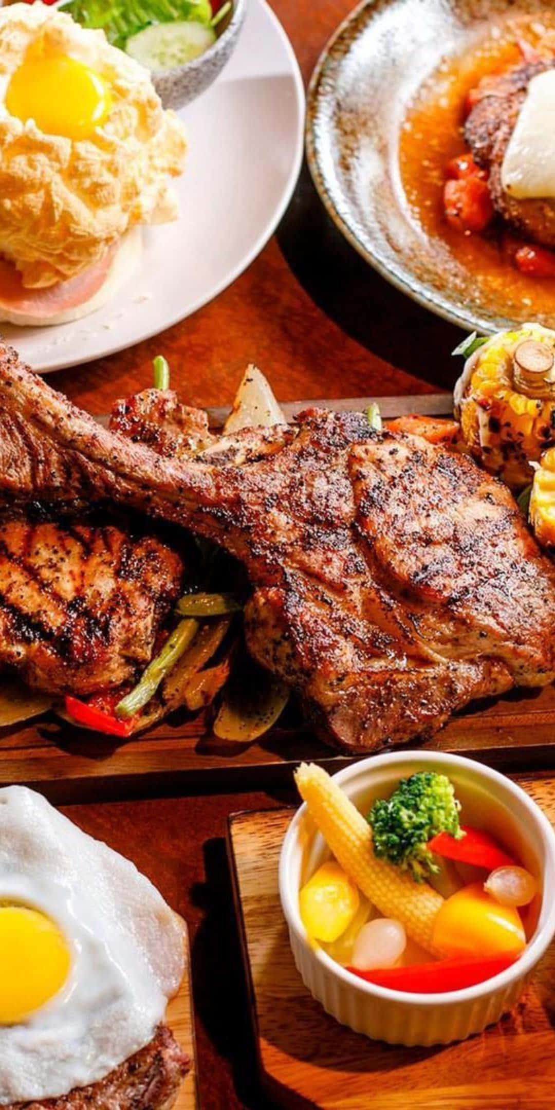 Pixel 3 食物牛排背景 壁紙 — 在質樸的木桌上，擺滿了帶骨烤牛排、太陽蛋和色彩繽紛的蔬菜配菜。