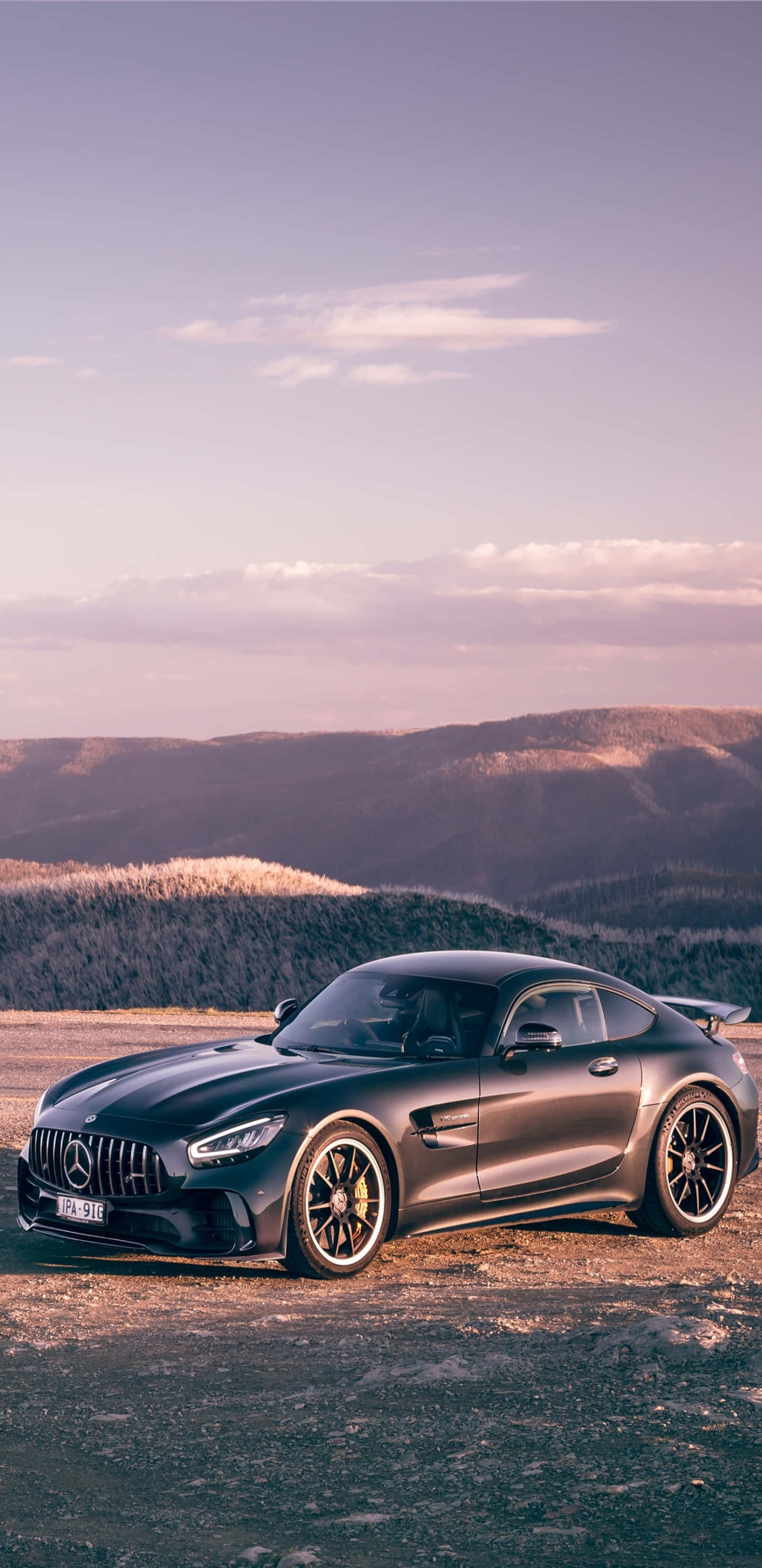 黑色梅賽德斯-奔馳配山景背景，適用於 Pixel 3XL AMG GT-R 壁紙 — 一架流線型啞黑色Mercedes-AMG GT停泊在日落時分的山路上，背景是連綿起伏的山丘。