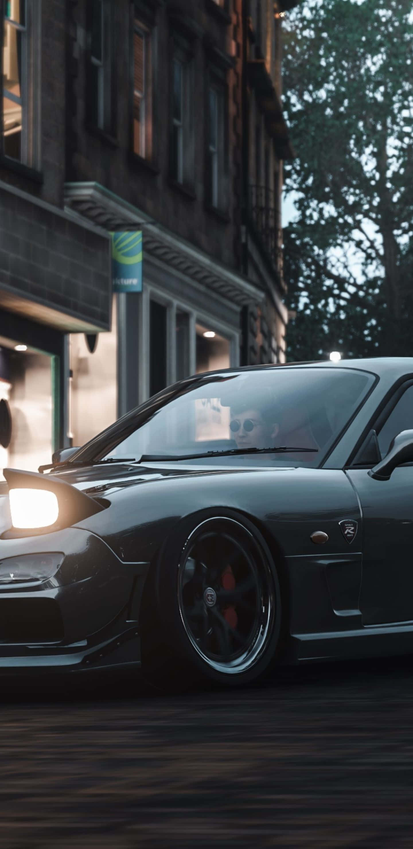 Pixel 3xl Forza Horizon 4 中夕陽下的絕美賽道 壁紙 — 一輛時尚的深灰色跑車，車頭燈閃閃發光，在黃昏時分載著戴太陽眼鏡的司機在城市的街道上飛馳。