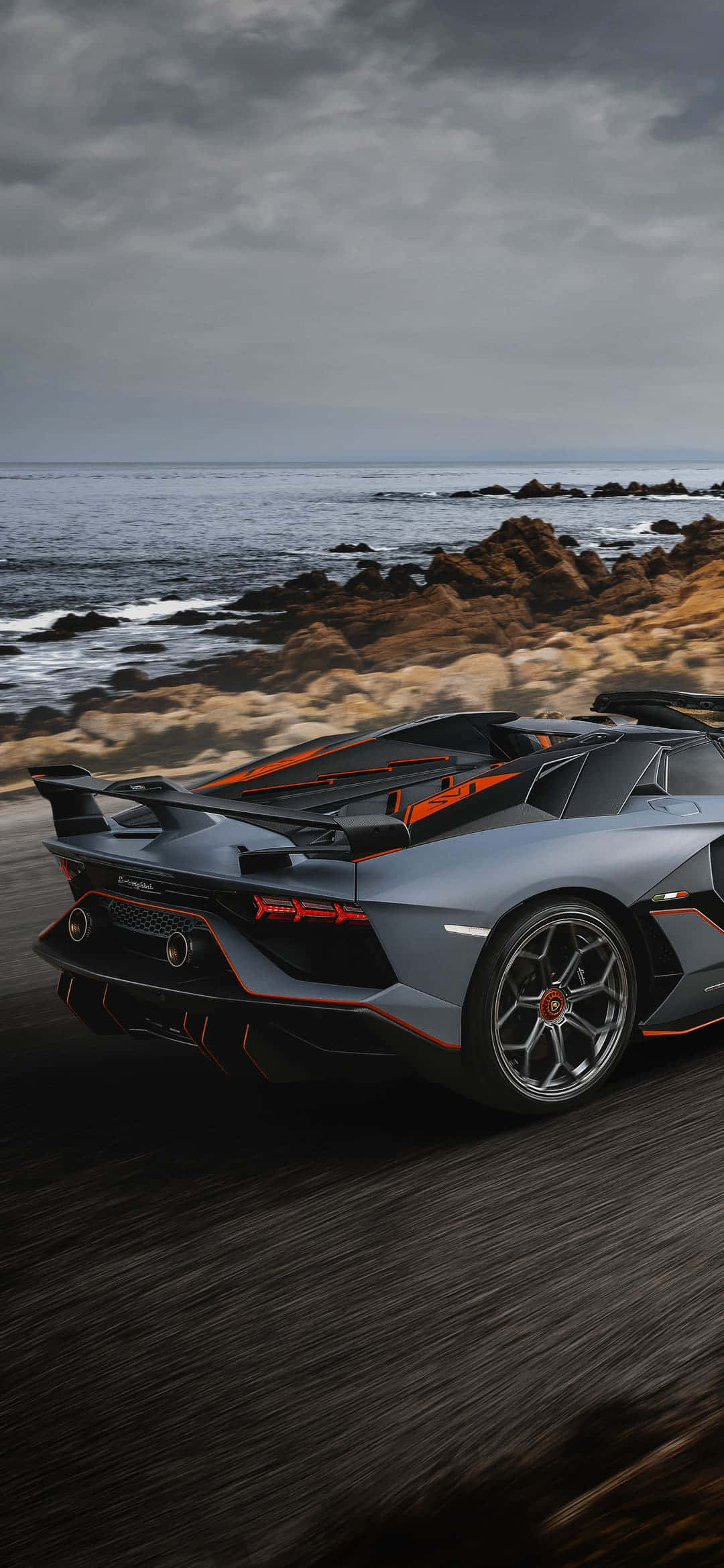 「夜幕主宰 — 新款 Pixel 3XL Lamborghini 版本」 壁紙 — 一輛帶有橙色點綴的時尚灰色林寶堅尼在暴風雨的天空下沿著海岸公路飛馳。