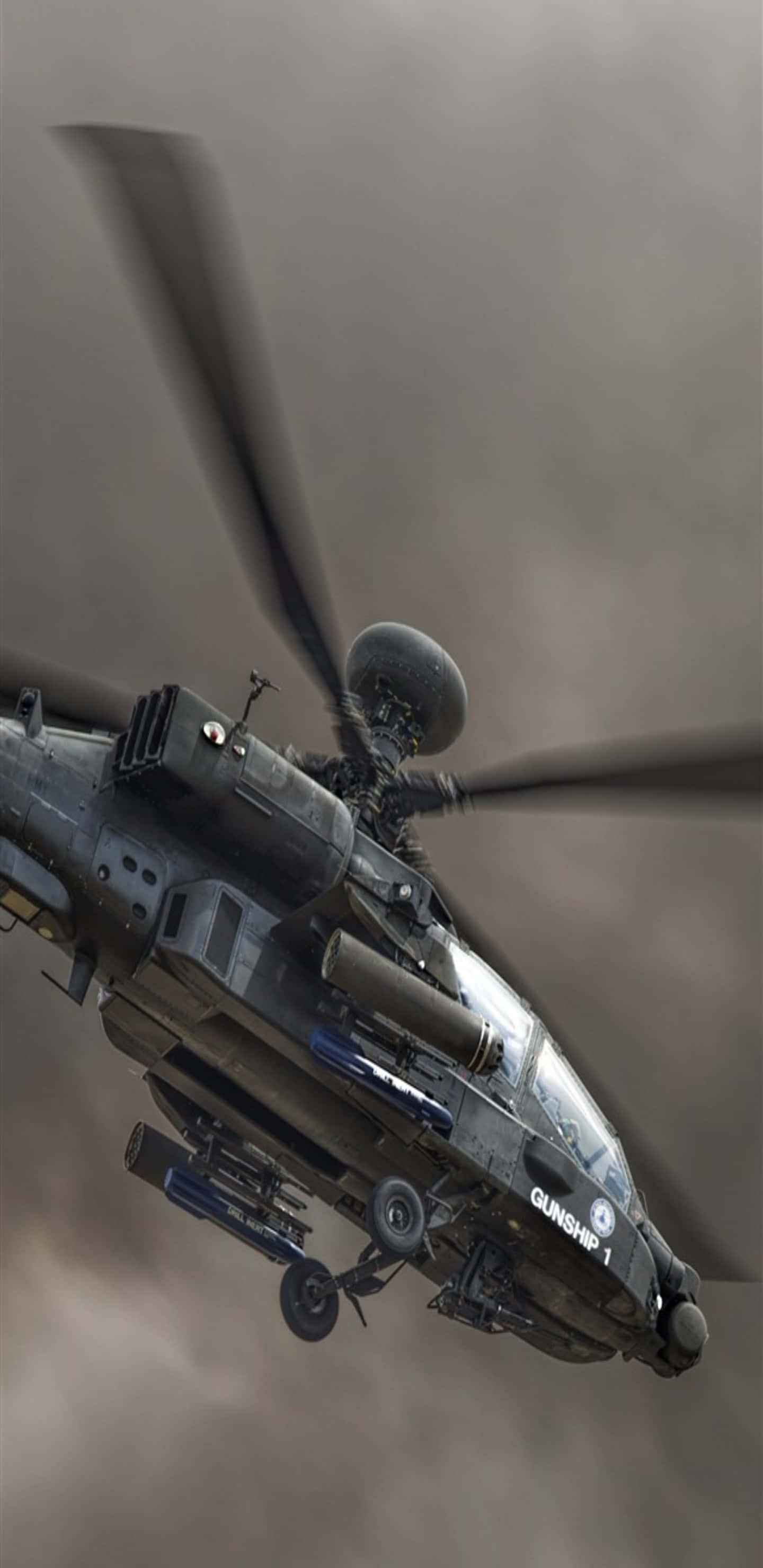 Pixel 3XL 直升機背景 Boeing AH-64 Apache 飛越烏雲 壁紙 — 一架軍用攻擊直升機在灰濛濛的天空中翱翔，旋轉的葉片和安裝的武器清晰可見。