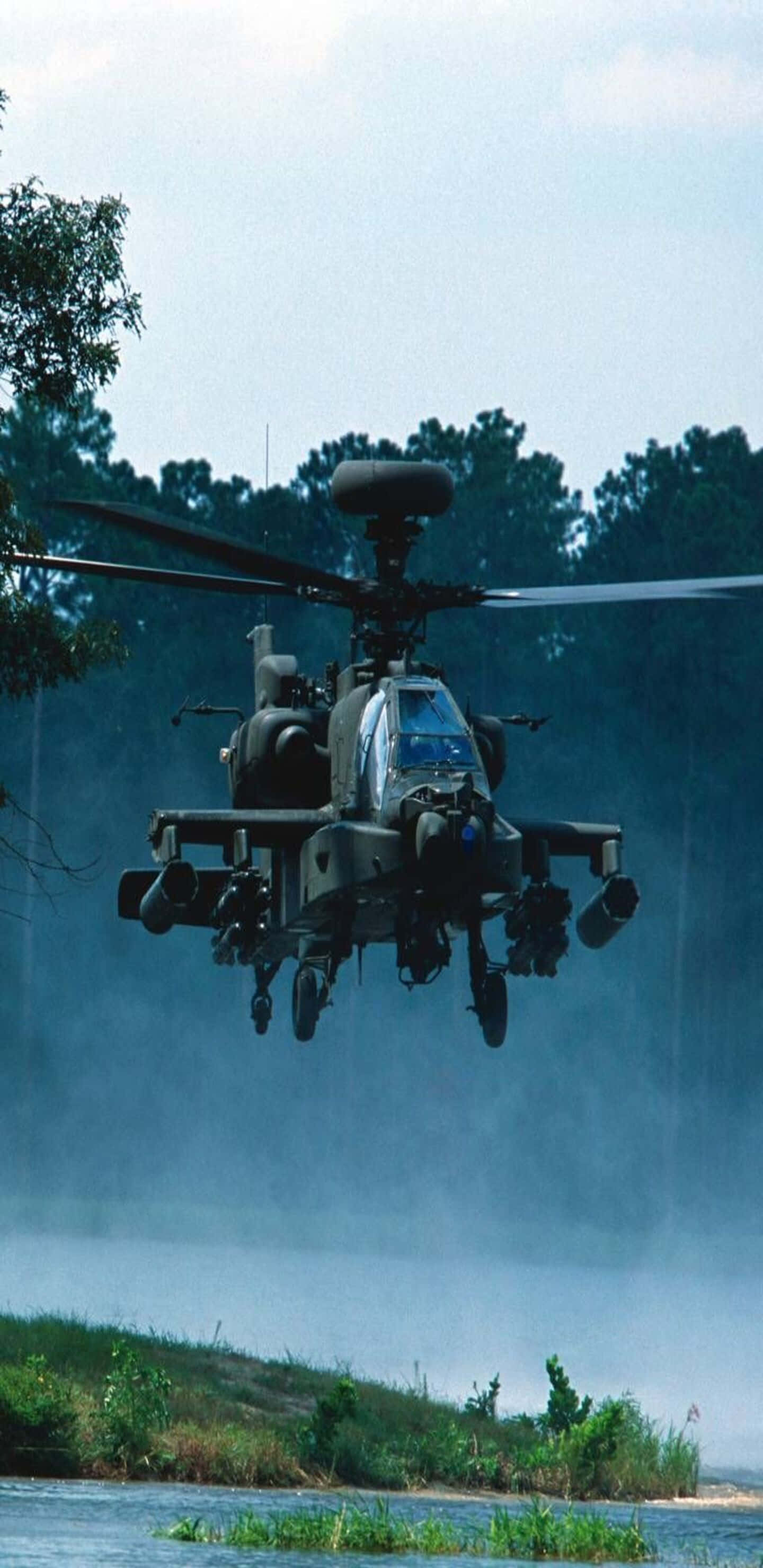 Pixel 3XL 直升機背景 Boeing AH-64 Apache 壁紙 — 一架軍用直升機低空盤旋於霧氣瀰漫的河流之上，背景是茂密的綠色樹木。