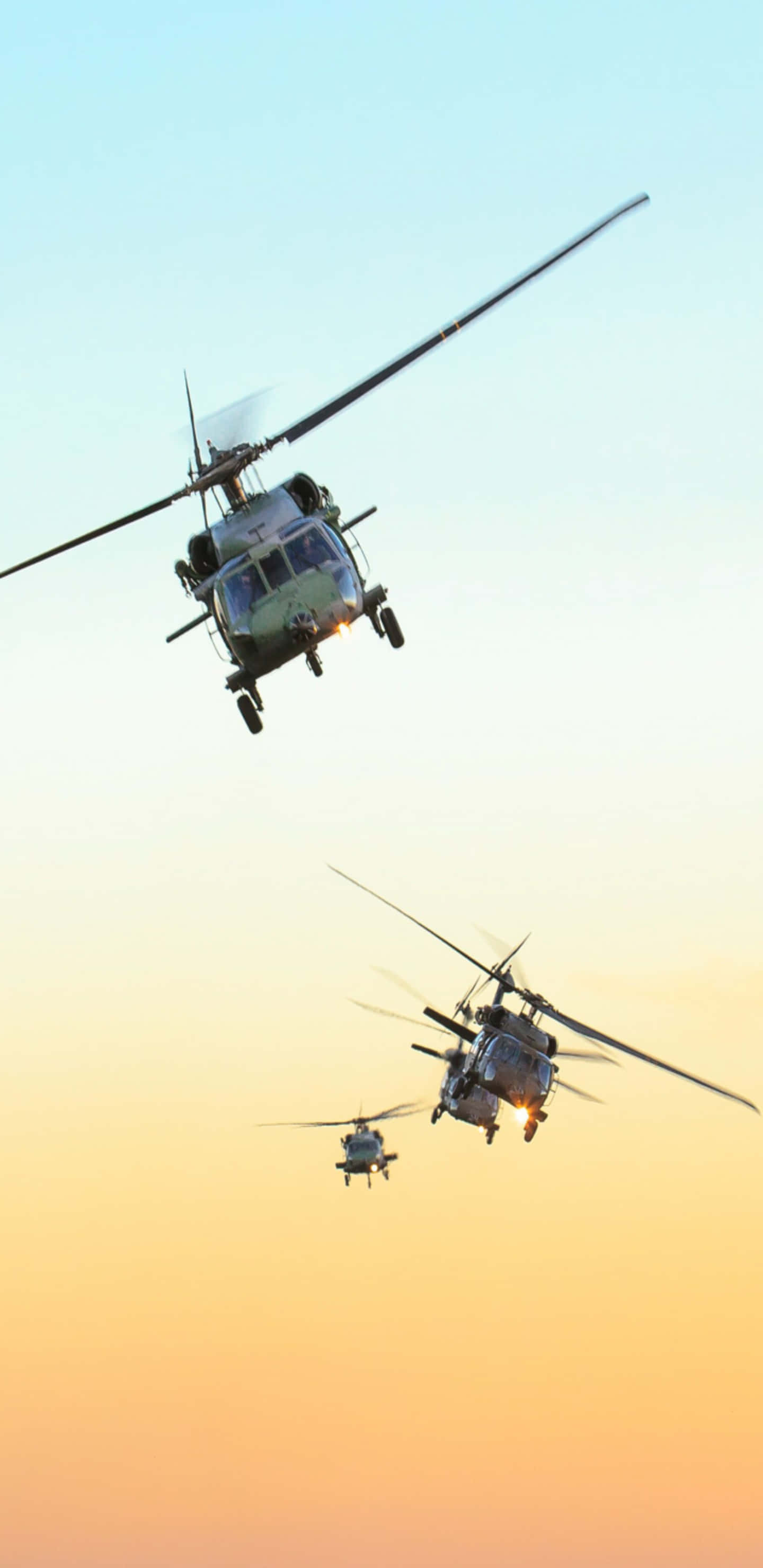 Pixel 3XL 背景：三架 Sikorsky UH-60 Black Hawk 直昇機 壁紙 — 三架軍用直升機在漸變色日落天空（溫暖橙色和冷藍色調）前編隊飛行。