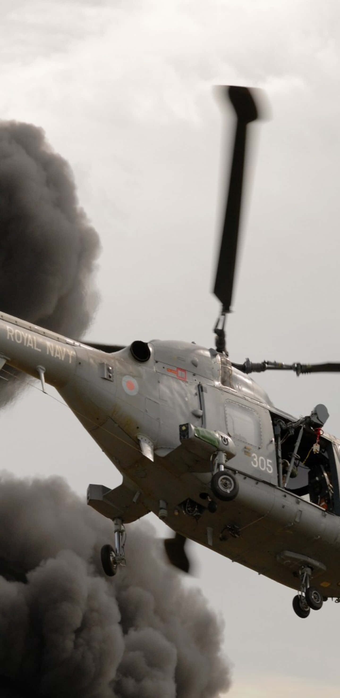 Pixel 3XL 背景：灰色西科斯基 UH-60 黑鷹直升機 壁紙 — 一架英國皇家海軍直升機在多雲的天空下低飛穿過濃厚的黑煙。
