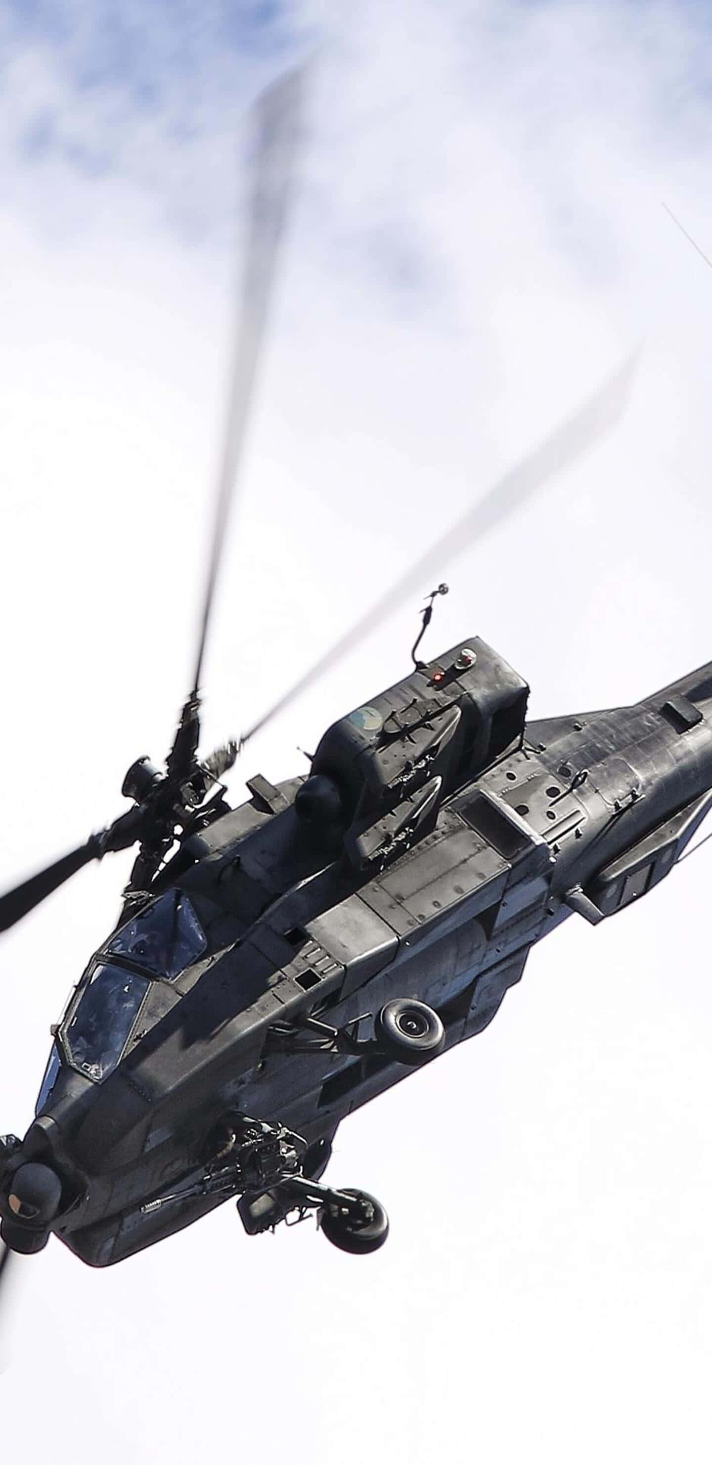 Pixel 3XL 背景：灰雲晴空下的 Boeing AH-64 Apache 直昇機 壁紙 — 一架流線型黑色軍用直升機在明亮的多雲天空中翱翔，旋轉的葉片產生動態模糊效果。