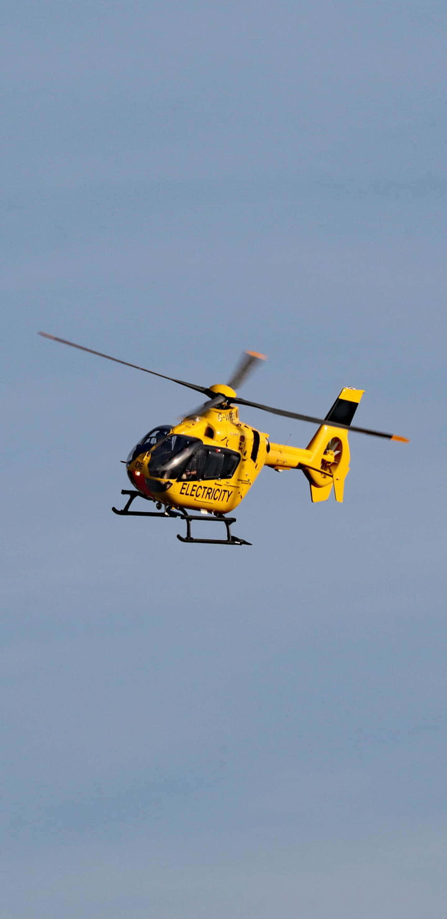 Pixel 3XL 背景：黃色歐直 EC135 直升機 壁紙 — 一架亮黃色的電力直升機在晴朗的藍天中翱翔，旋翼轉動。