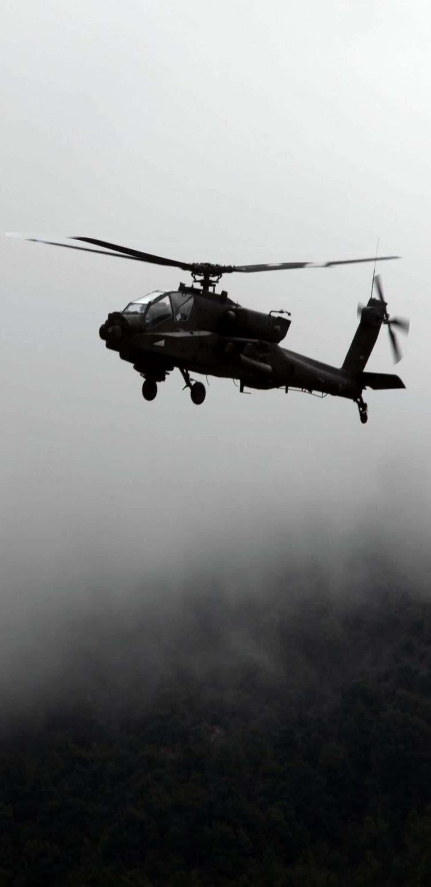 Pixel 3XL 背景：黑白 Boeing AH-64 Apache 直昇機 壁紙 — 一架深色軍用直升機以單色調低飛過霧氣籠罩的森林樹冠。