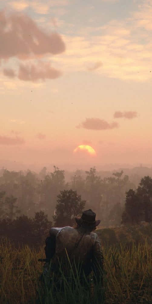 一個戴帽的牛仔看著夕陽在樹木繁茂的地平線上落下。
