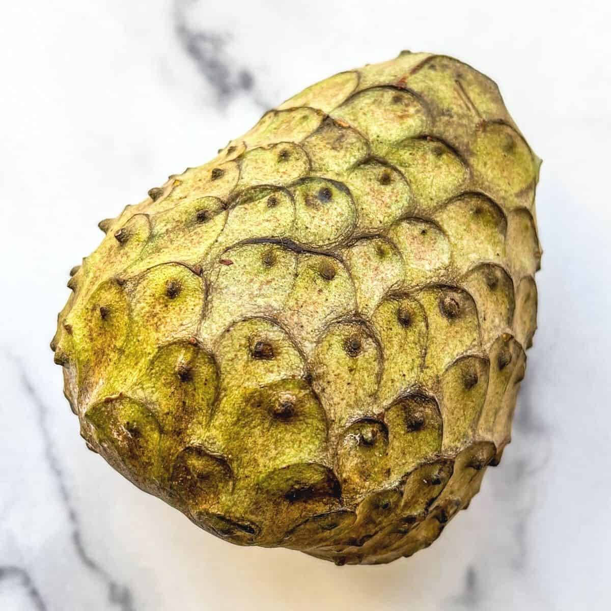 Platone 品種奇異果 壁紙 — 一個帶刺的綠色刺果番荔枝果實的特寫，放在白色大理石表面上。