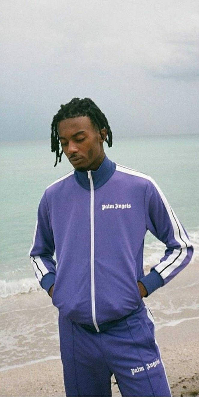 身穿紫色運動服的男子站在海灘上，身後有海浪