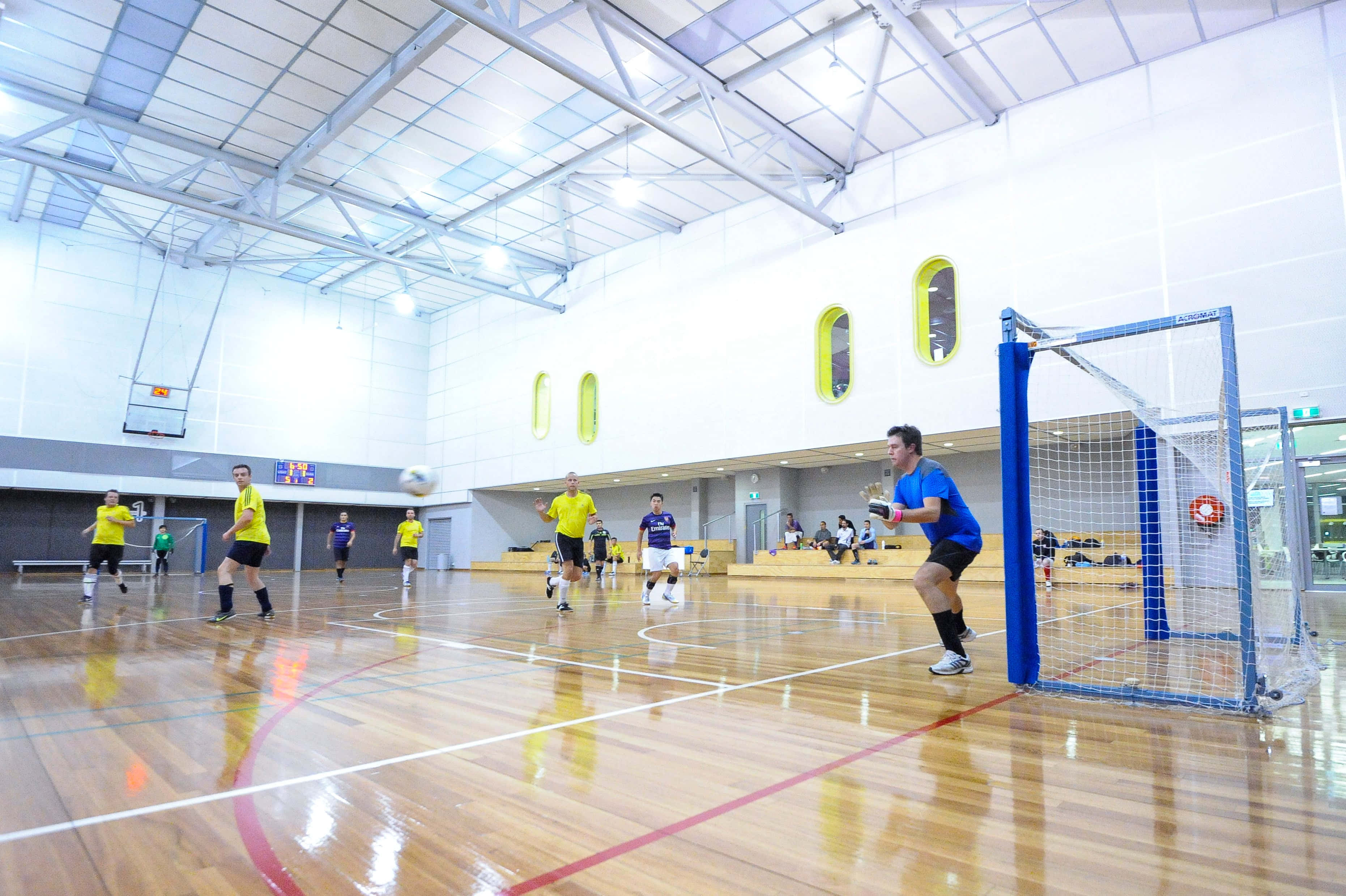 Indoor Soccer 桌布 壁紙 — 球員在明亮的燈光下於拋光木地板上進行室內足球比賽。