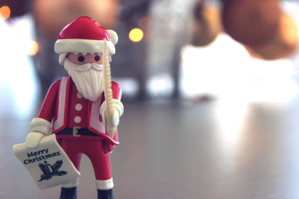Santa Claus 桌布 壁紙 — Playmobil 聖誕老人公仔的特寫，手持「聖誕快樂」標誌，背景柔和溫暖模糊。